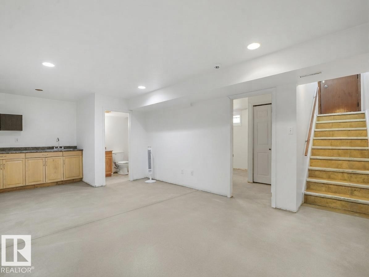 Recessed lighting illuminates the open area, featuring light wood-finish cabinetry, a sink, and a dark countertop - 16428 88 Avenue Nw, Edmonton, AB