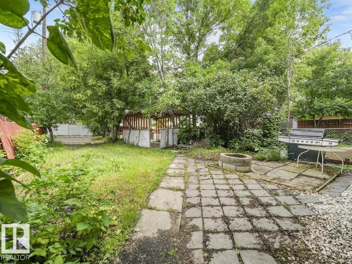 Expansive backyard featuring a stone paver patio, gravel hardscaping, a block fire pit, and mature trees - 16428 88 Avenue Nw, Edmonton, AB