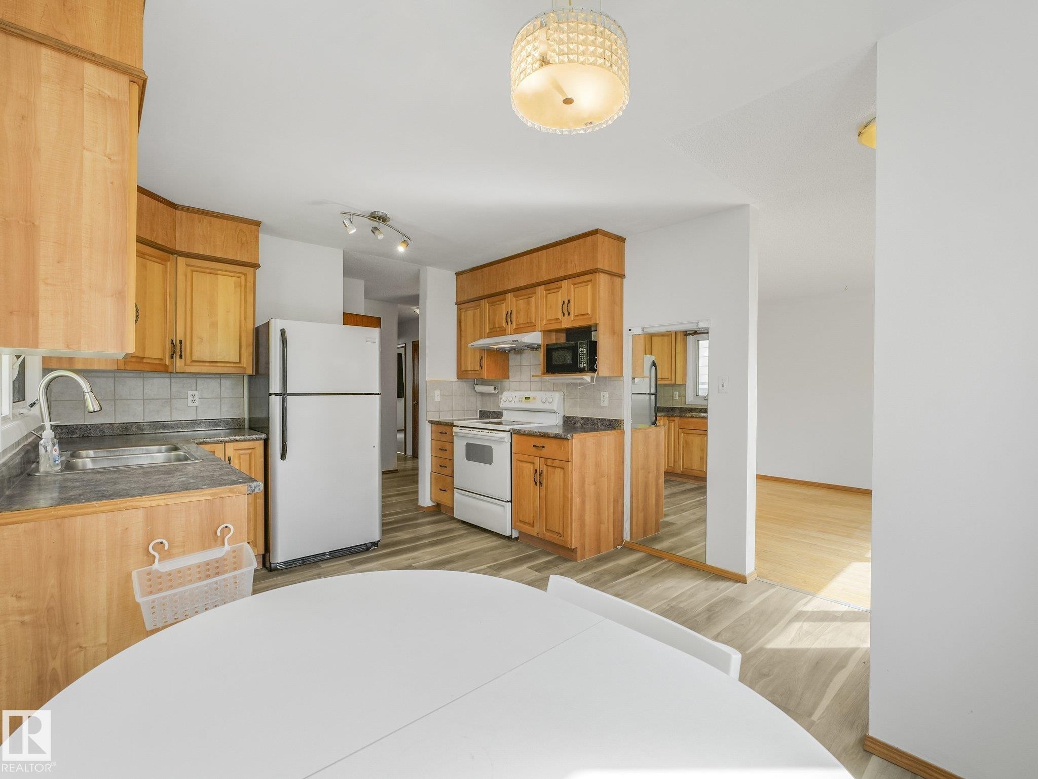 Kitchen featuring wood cabinetry, a double basin sink, white appliances, and wood-finish flooring - 16428 88 Avenue Nw, Edmonton, AB