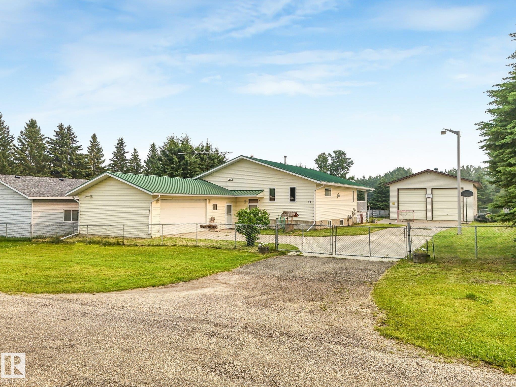 Spacious property featuring a light-toned exterior with a green metal roof, a fenced perimeter, a gravel driveway, and an additional detached two-stall garage - 54 Buskmose Dr, Rural Wetaskiwin County, AB - Outdoor