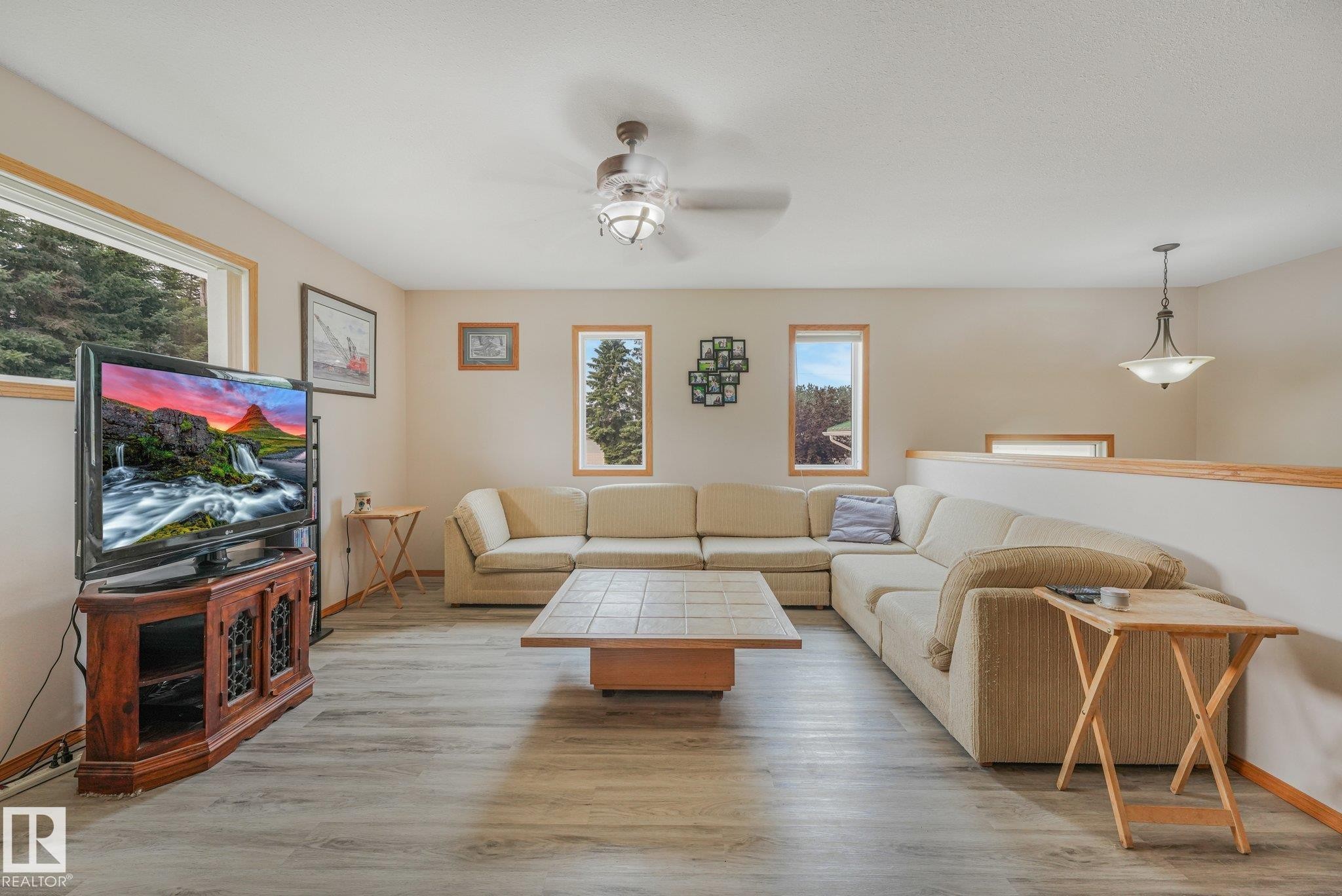 Spacious living area featuring wood-finish flooring and multiple windows with wood trim - 54 Buskmose Dr, Rural Wetaskiwin County, AB - Indoor Photo Showing Living Room