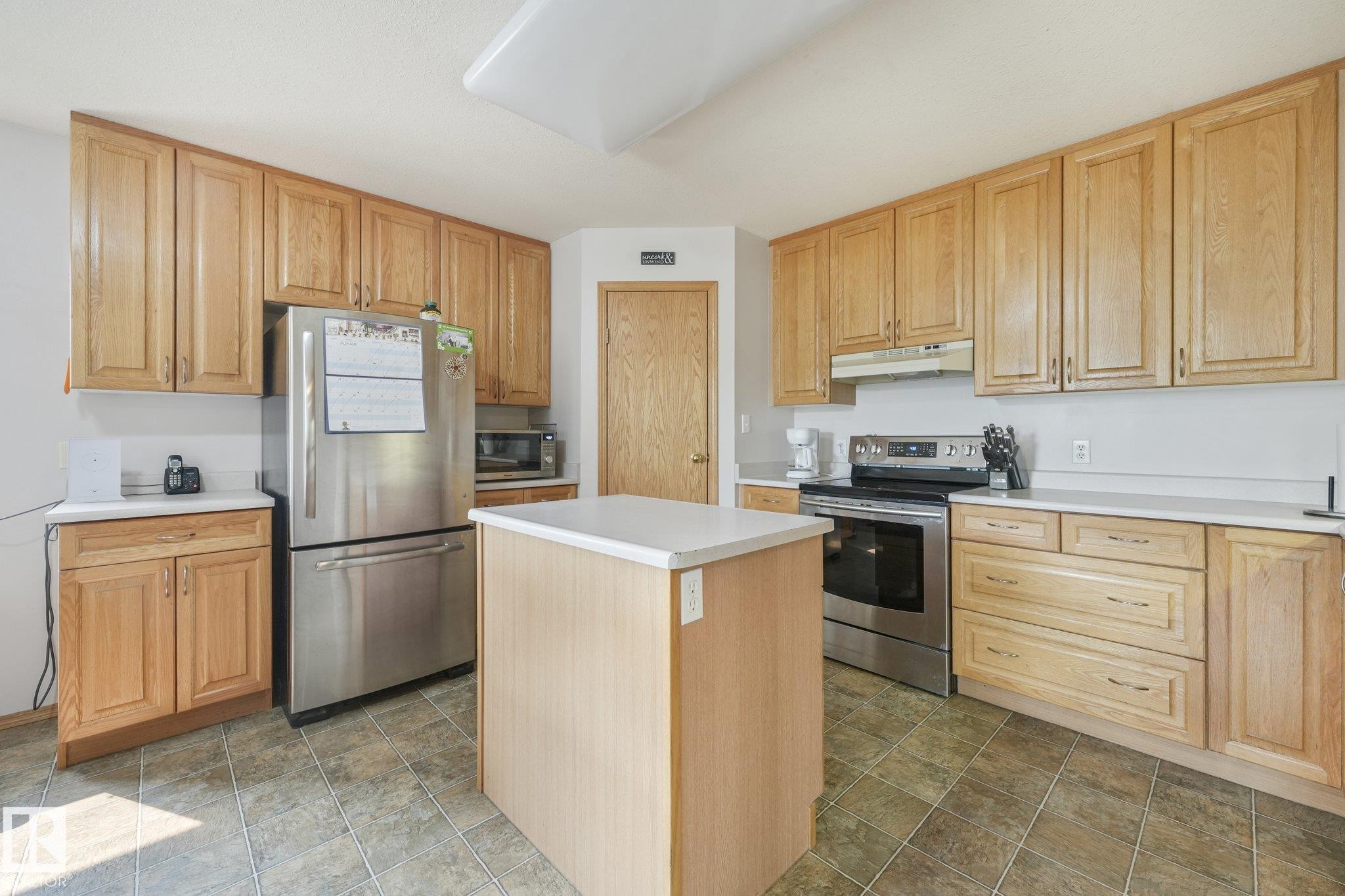 Kitchen featuring wood cabinetry with ample storage, stainless steel appliances, a central island with countertop, and tile flooring - 54 Buskmose Dr, Rural Wetaskiwin County, AB - Indoor Photo Showing Kitchen