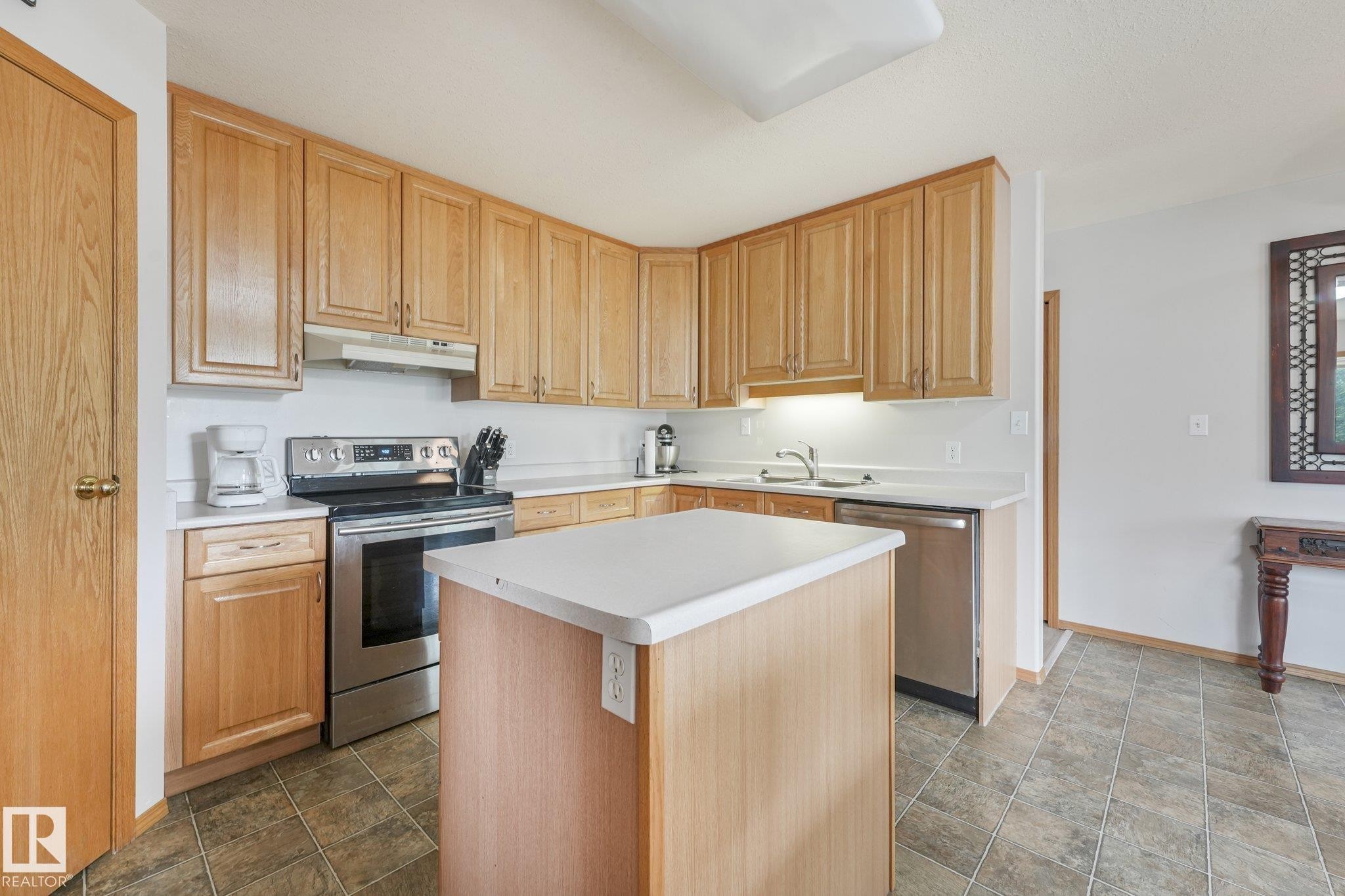 Kitchen featuring wood cabinetry, stainless steel appliances, a center island with a white countertop, and tiled flooring - 54 Buskmose Dr, Rural Wetaskiwin County, AB - Indoor Photo Showing Kitchen With Double Sink