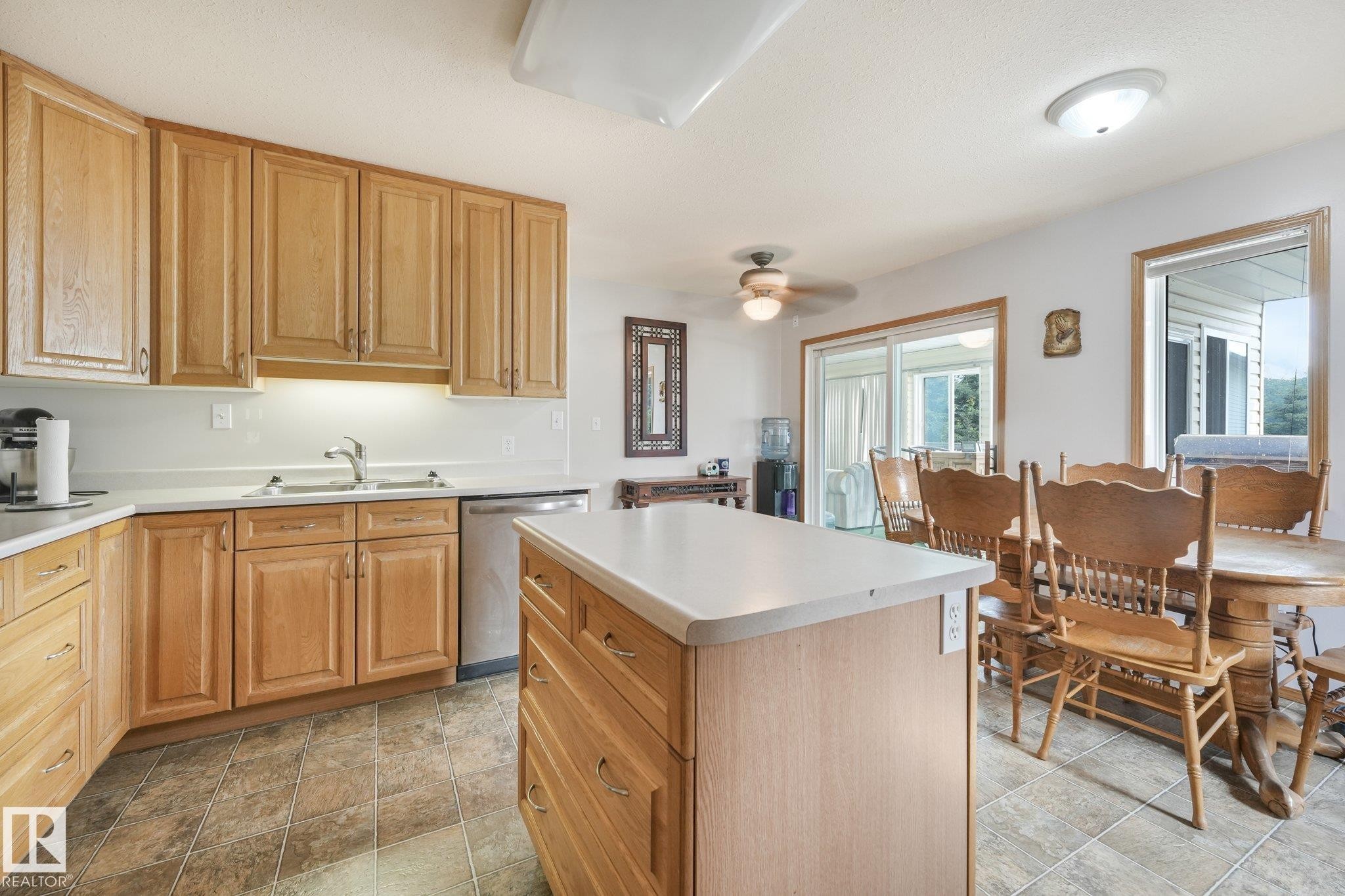 Kitchen featuring wood cabinetry, white countertops, tile flooring, a stainless steel dishwasher, and a center island with storage - 54 Buskmose Dr, Rural Wetaskiwin County, AB - Indoor Photo Showing Kitchen With Double Sink