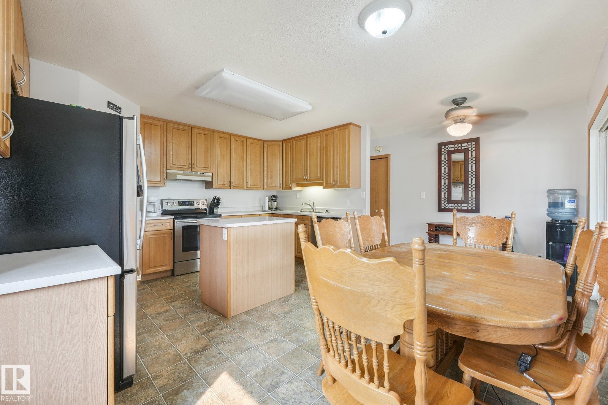 Kitchen and dining area featuring wood-finish cabinetry, stainless steel appliances, a center island with countertop, and tile flooring - 54 Buskmose Dr, Rural Wetaskiwin County, AB - Indoor
