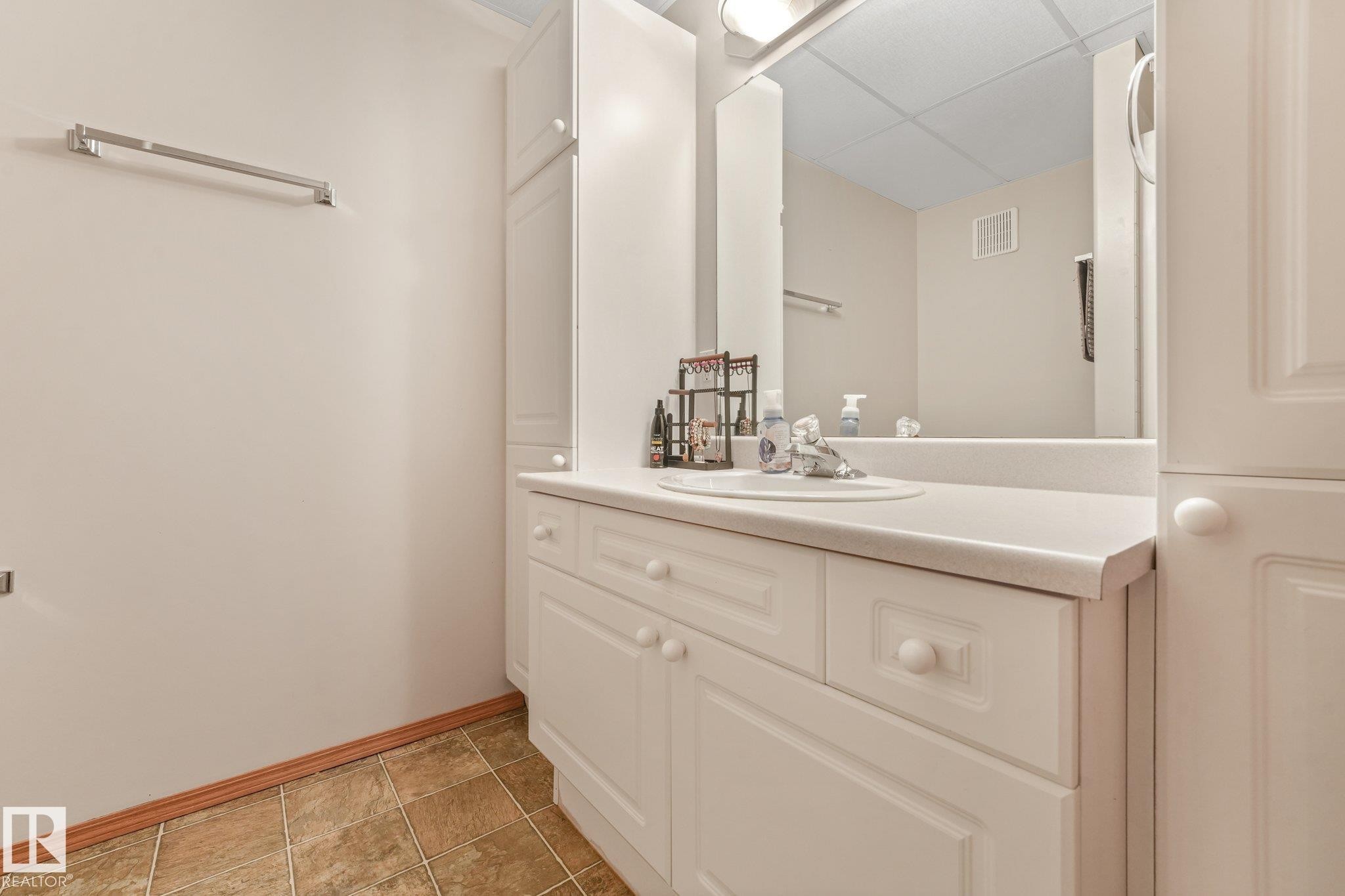 White cabinetry vanity with integrated sink and countertop, framed by a large mirror with overhead lighting - 54 Buskmose Dr, Rural Wetaskiwin County, AB - Indoor Photo Showing Bathroom