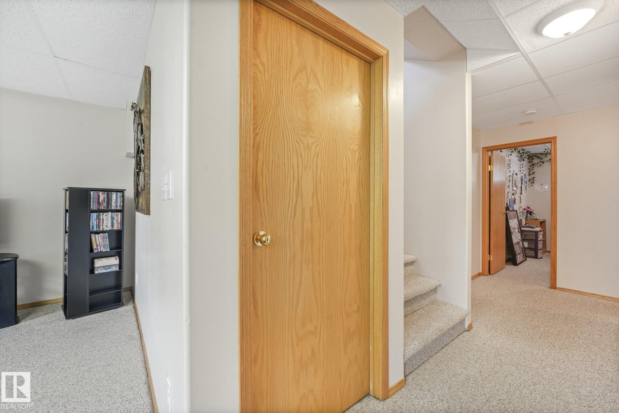 Carpeted hallway with a light wood-finish door, matching trim, and a drop ceiling with recessed lighting - 54 Buskmose Dr, Rural Wetaskiwin County, AB - Indoor Photo Showing Other Room