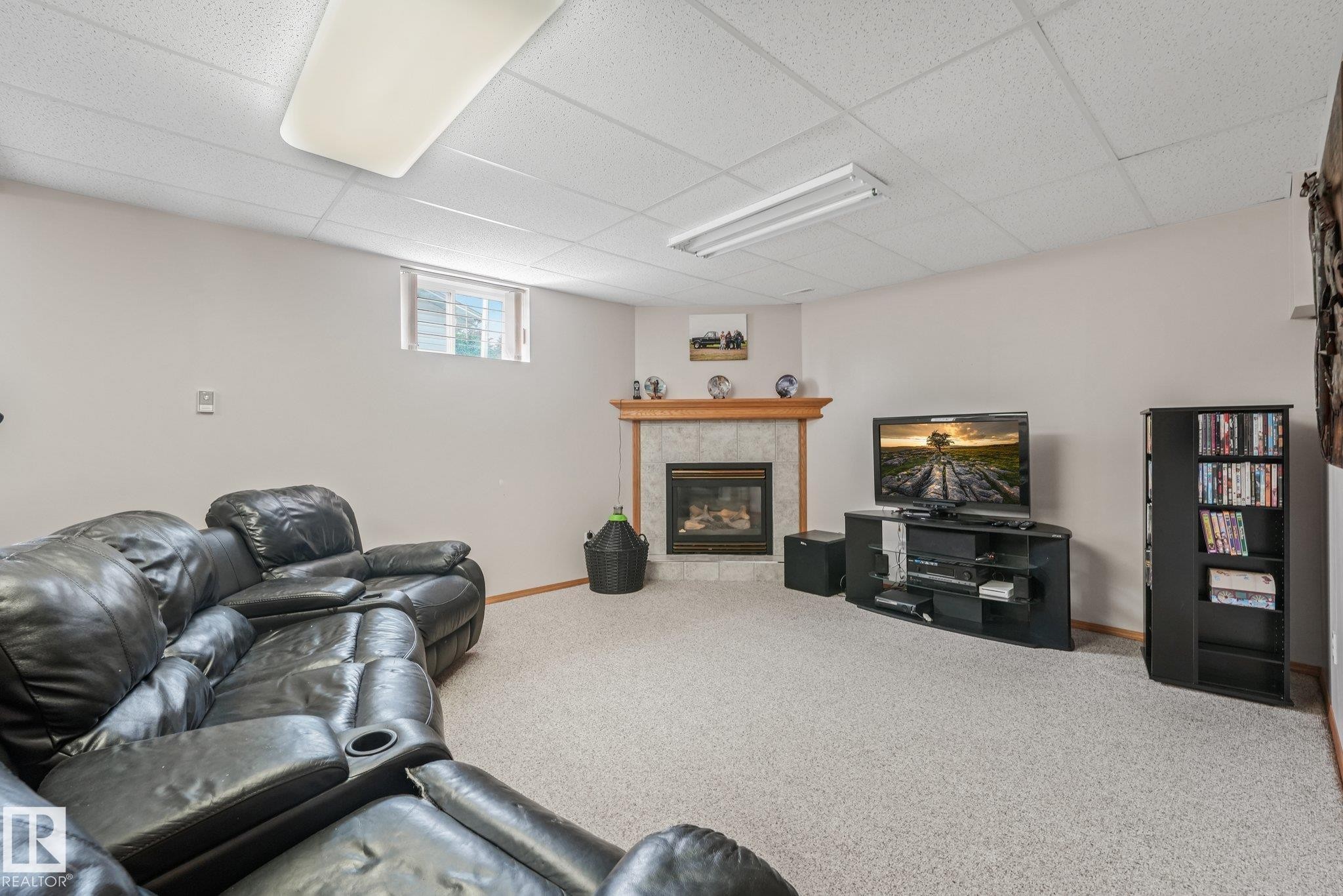 Corner fireplace with stone tile surround and wood mantel - 54 Buskmose Dr, Rural Wetaskiwin County, AB - Indoor Photo Showing Basement With Fireplace