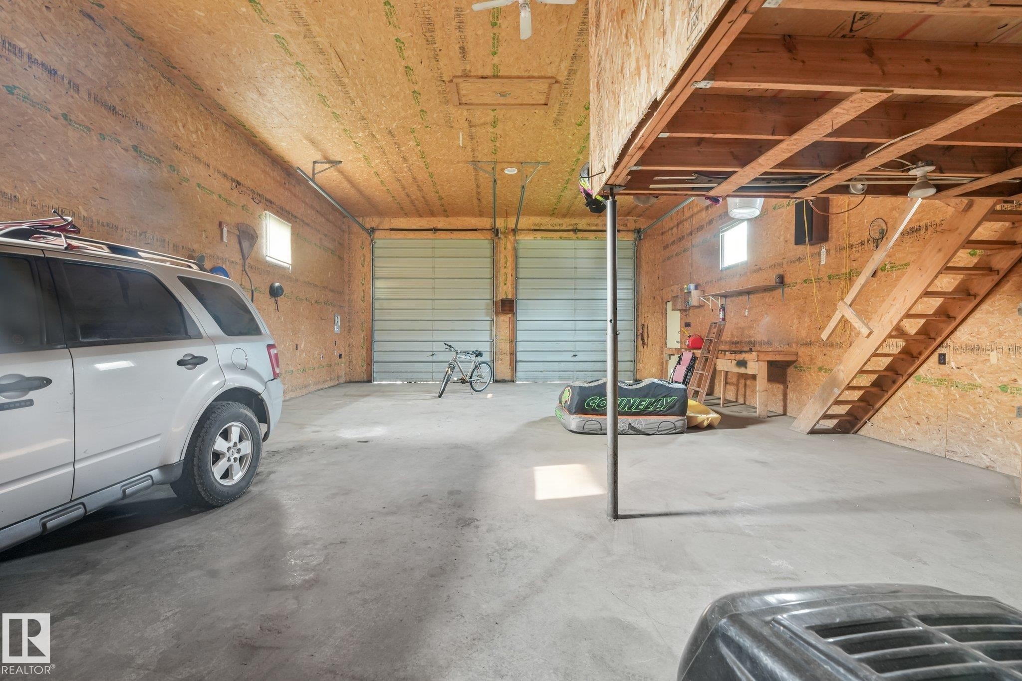 Spacious garage with concrete flooring, two roll-up doors, and exposed wood-finish walls - 54 Buskmose Dr, Rural Wetaskiwin County, AB - Indoor Photo Showing Garage
