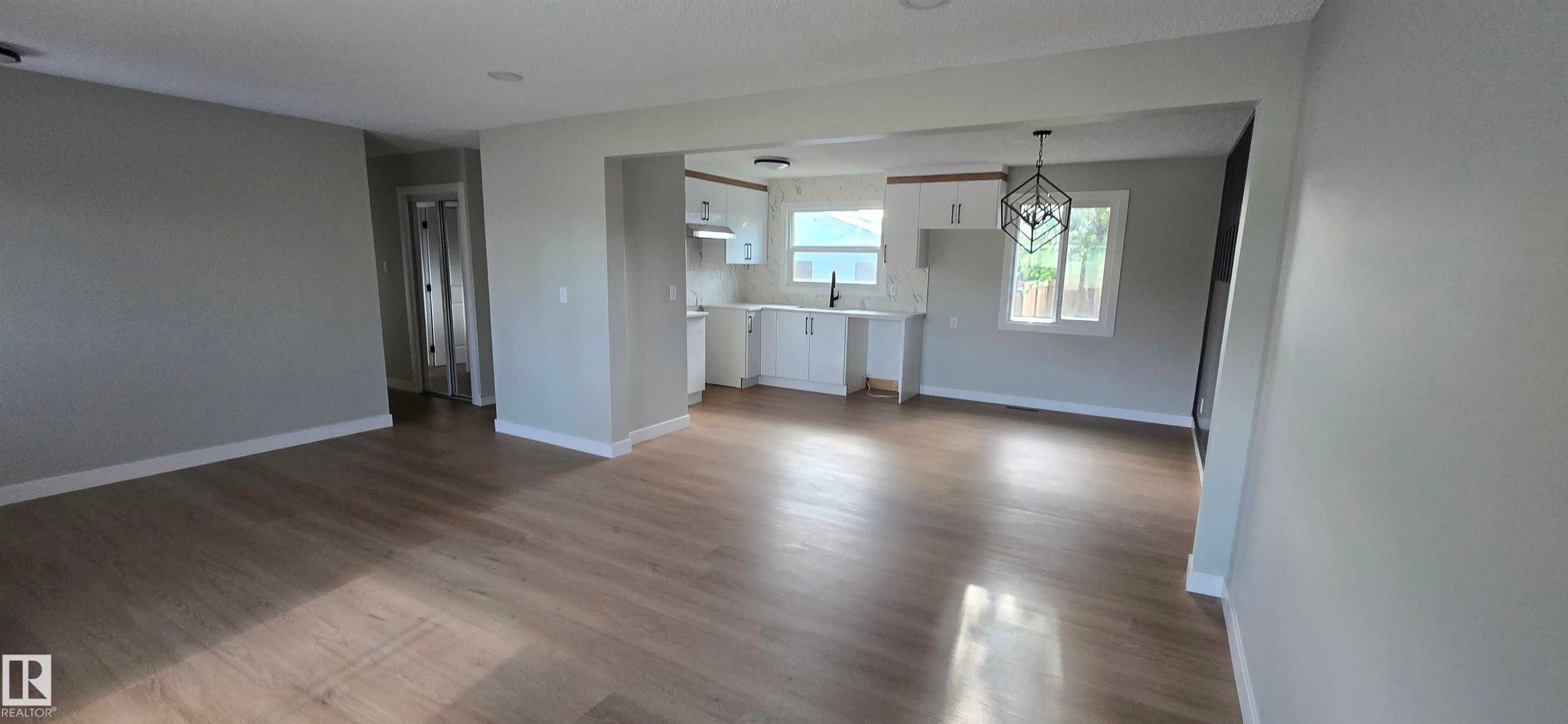 Open-concept layout with wood-finish flooring, white kitchen cabinetry, recessed lighting, and a modern geometric pendant light fixture - 13812 63 Street Nw, Edmonton, AB
