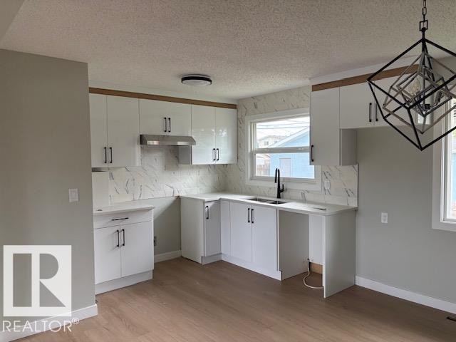 Contemporary kitchen featuring white cabinetry, a black faucet, a stainless steel range hood, stone-finish countertops, and wood-finish flooring - 13812 63 Street Nw, Edmonton, AB