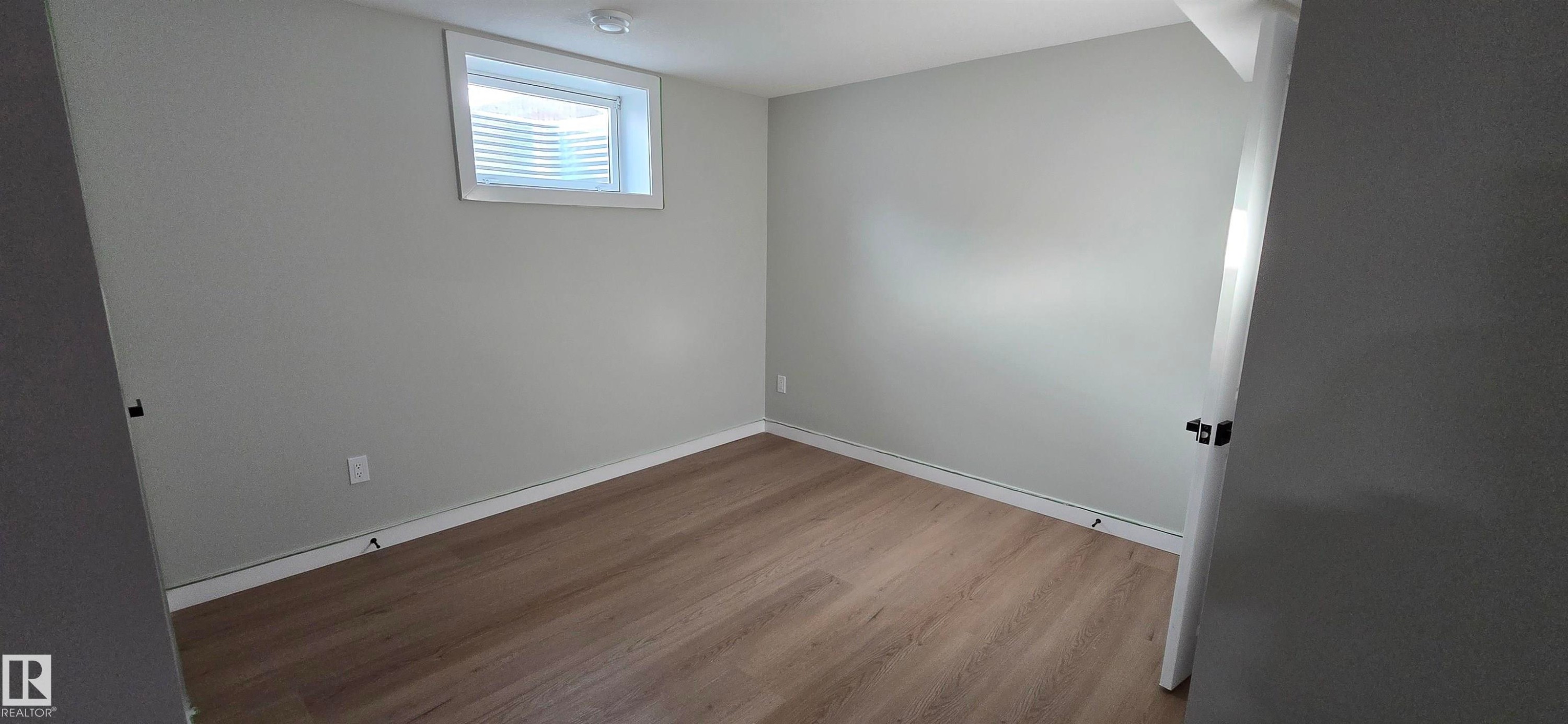 Light grey walls, wood-finish flooring, white window trim, and a flush-mount ceiling light - 13812 63 Street Nw, Edmonton, AB