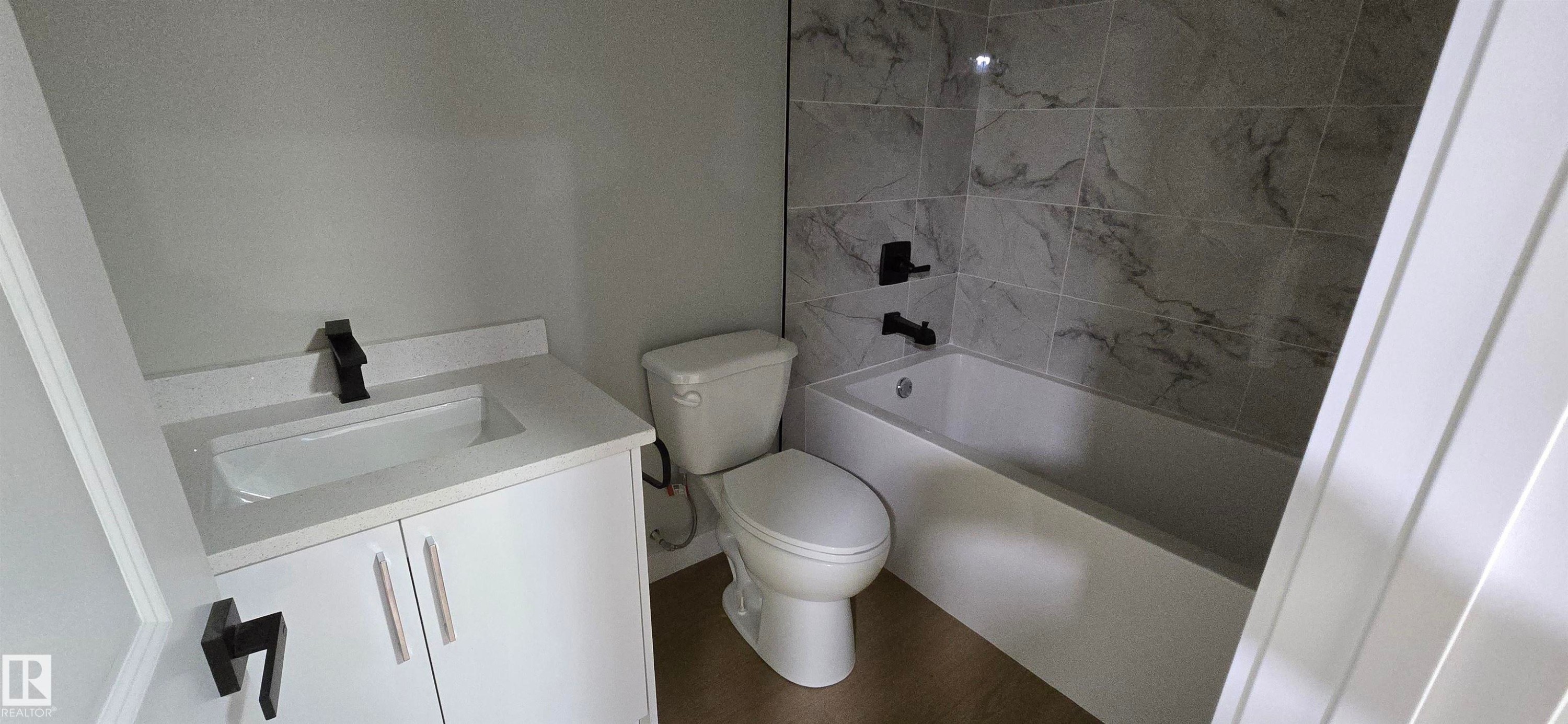 Bathroom featuring a white vanity with integrated sink, matte black faucet, and a tiled shower-over-tub with matte black fixtures - 13812 63 Street Nw, Edmonton, AB