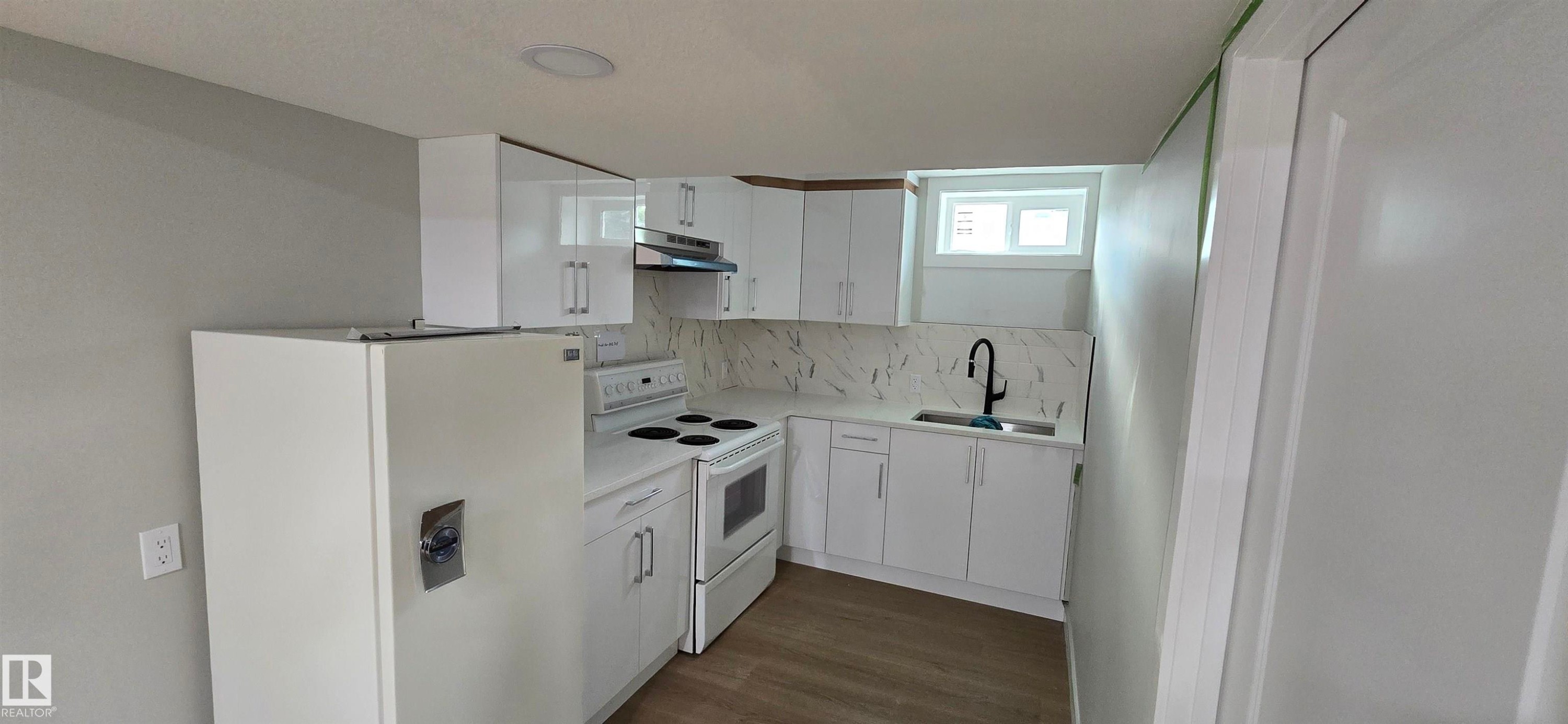 Modern kitchen featuring white cabinetry, a black faucet, a built-in electric range, a refrigerator, and wood-finish flooring - 13812 63 Street Nw, Edmonton, AB