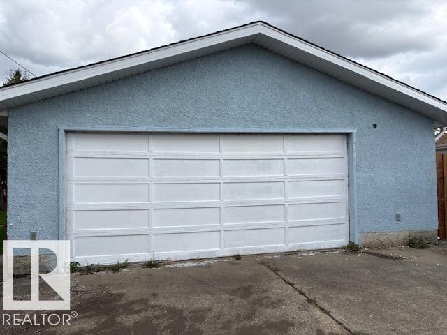 Attached garage featuring a panel-style door, textured exterior finish, and a sloped roofline - 13812 63 Street Nw, Edmonton, AB