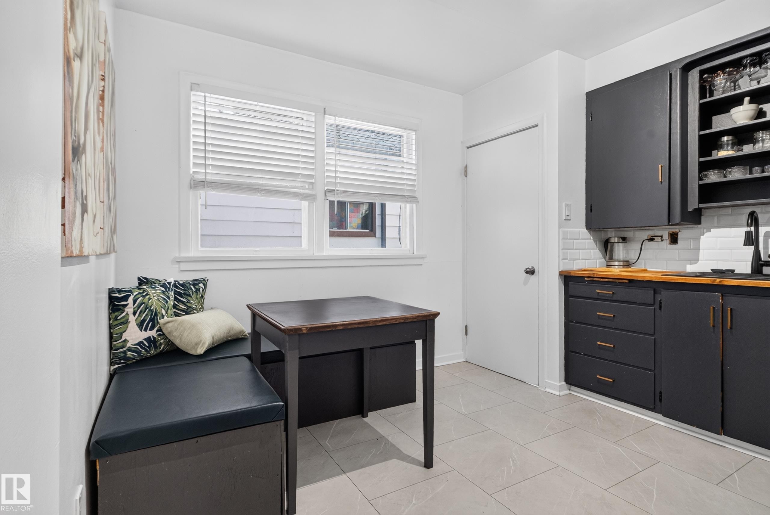 White subway tile backsplash, wood-finish countertops, black cabinetry with gold-tone hardware, light-toned tile flooring, and a built-in bench - 11406 83 Street Nw, Edmonton, AB