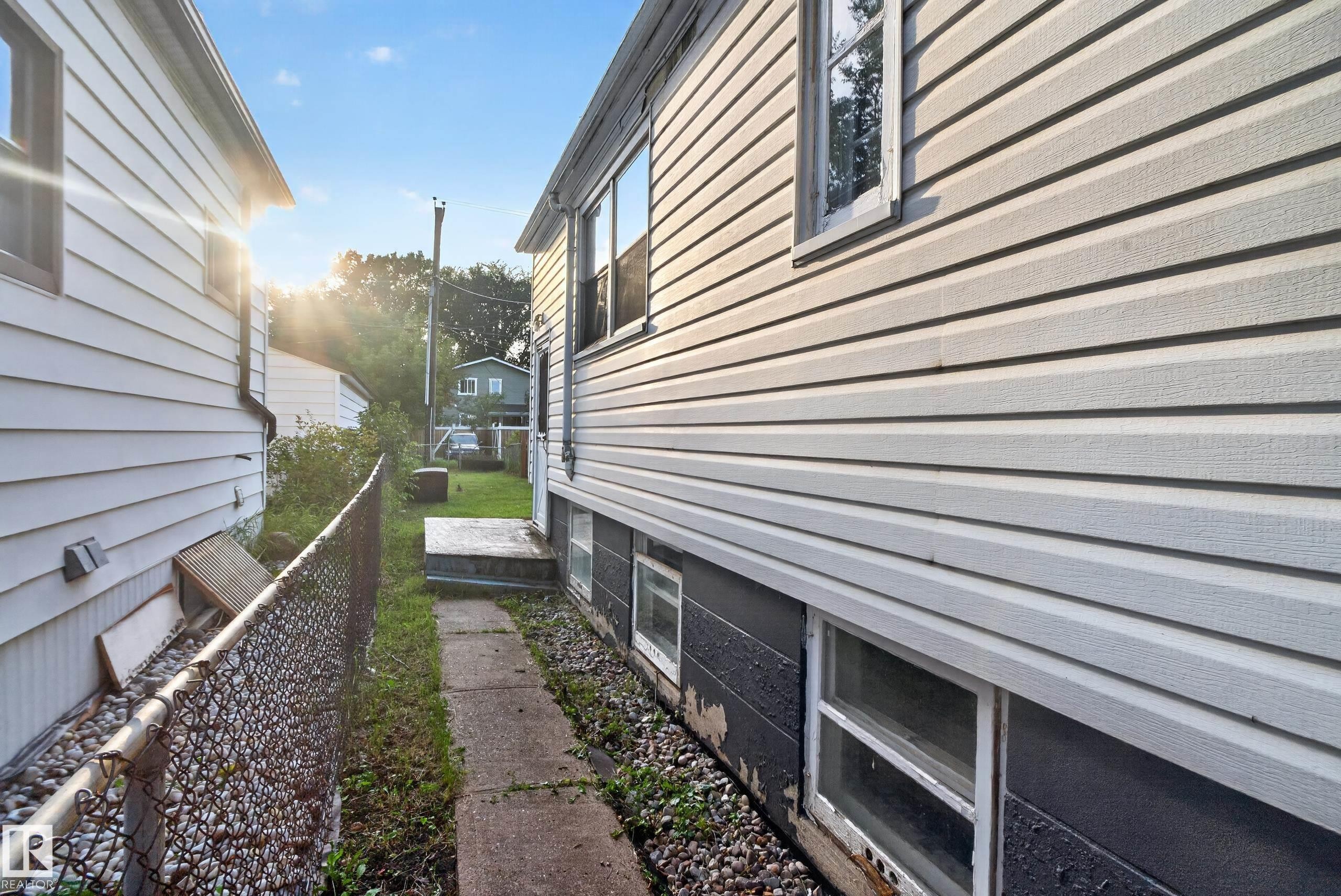 White vinyl siding, concrete pathway, chain-link fence, and lower-level windows - 11406 83 Street Nw, Edmonton, AB