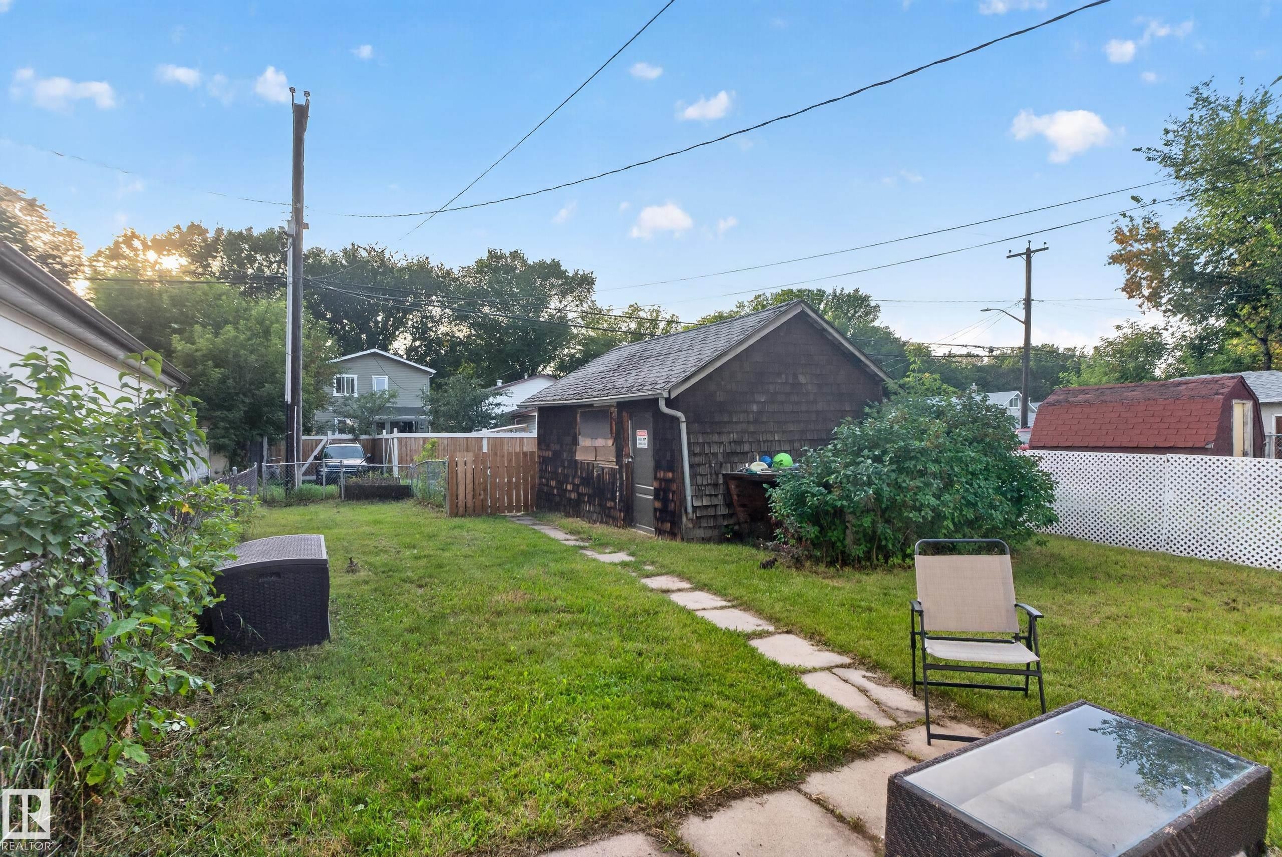 Expansive backyard featuring a stone paver pathway, a detached shed with wood shingle siding, and a white lattice fence - 11406 83 Street Nw, Edmonton, AB