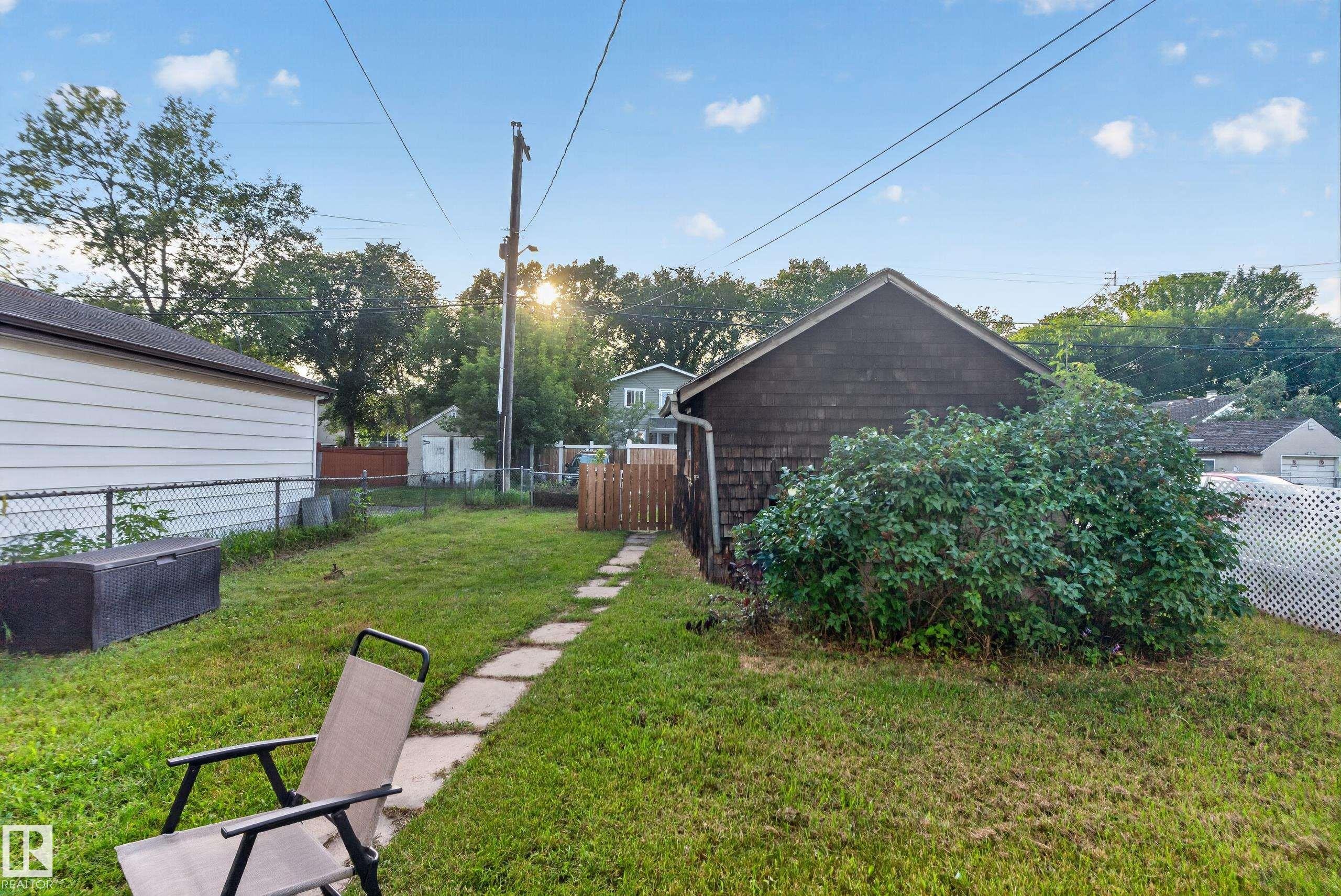 Expansive backyard featuring a stepping stone pathway, mature landscaping, chain link fencing, and a detached structure with shingle siding - 11406 83 Street Nw, Edmonton, AB