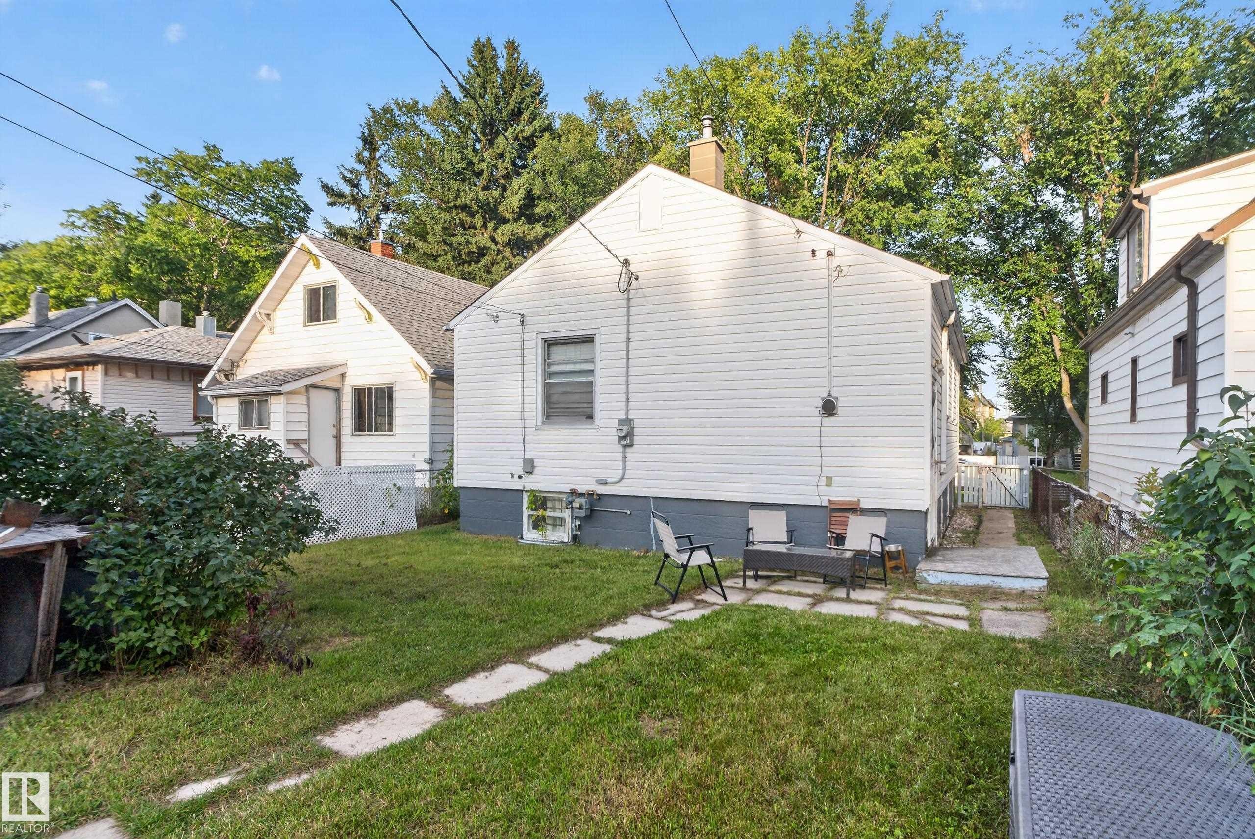Rear exterior featuring white siding, a stone patio, and a grass lawn - 11406 83 Street Nw, Edmonton, AB