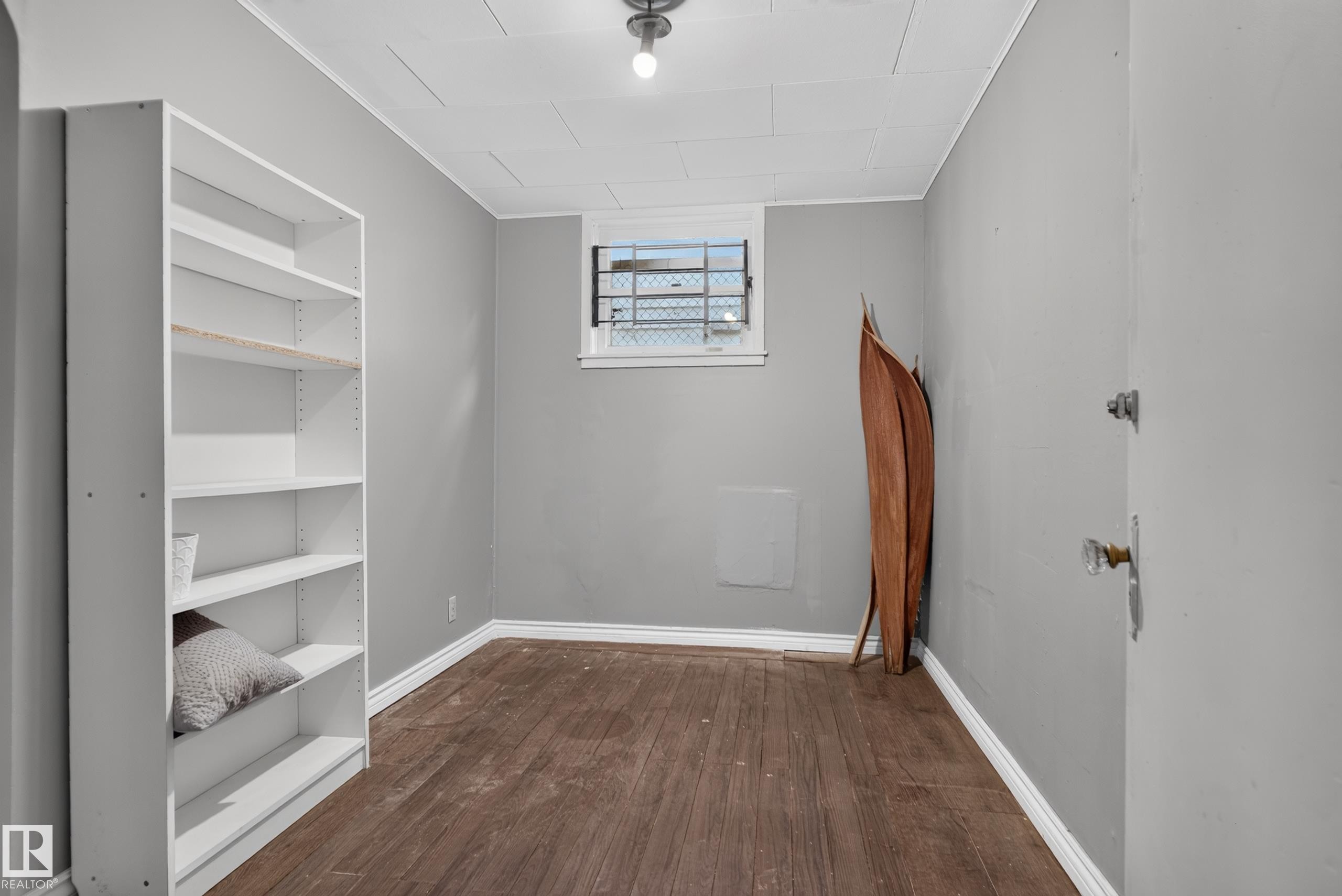 Wood-finish flooring, built-in shelving, window with security bars, and a flush mount ceiling light - 11406 83 Street Nw, Edmonton, AB
