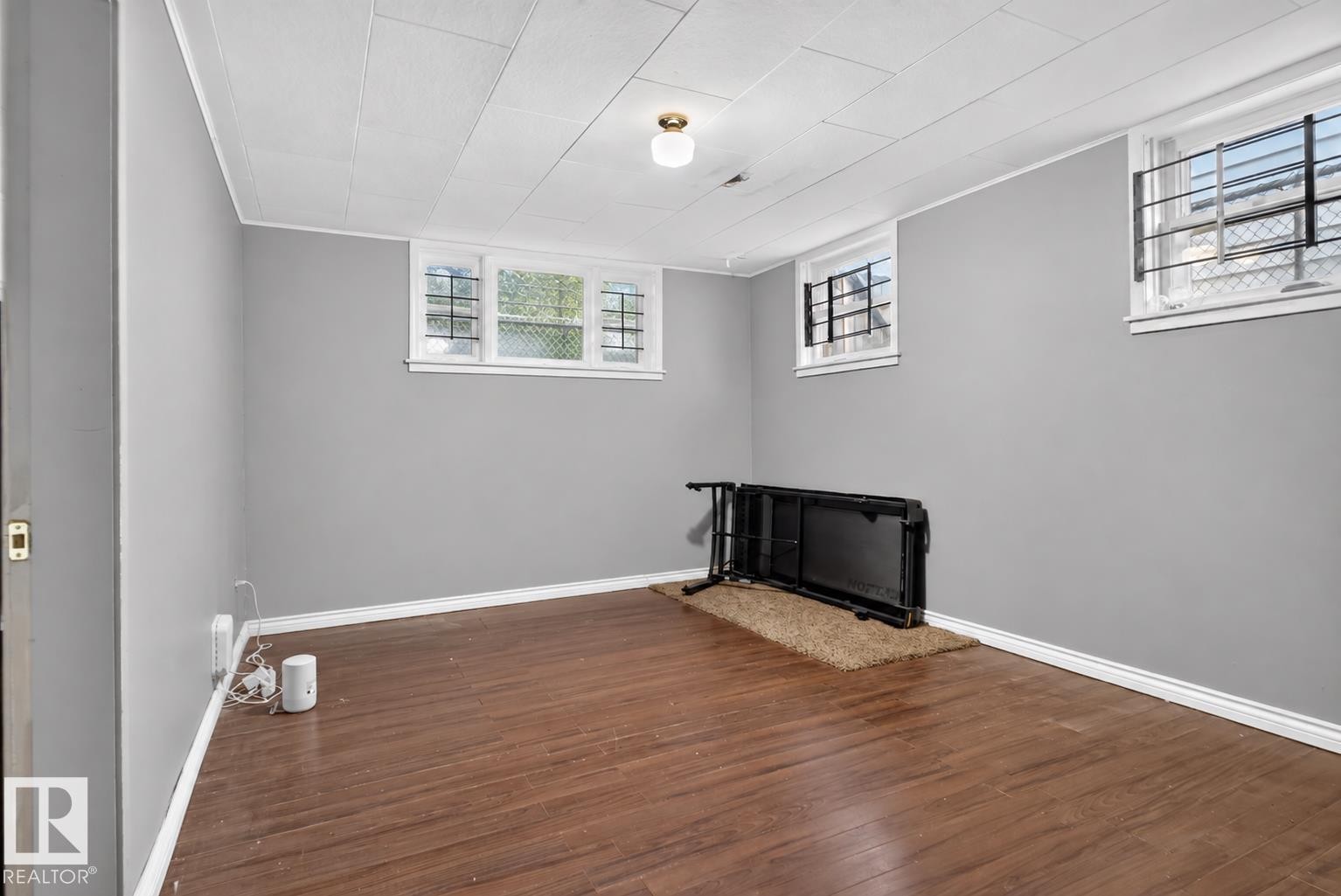 Wood-finish flooring, light gray wall paint, and multiple windows with security bars - 11406 83 Street Nw, Edmonton, AB