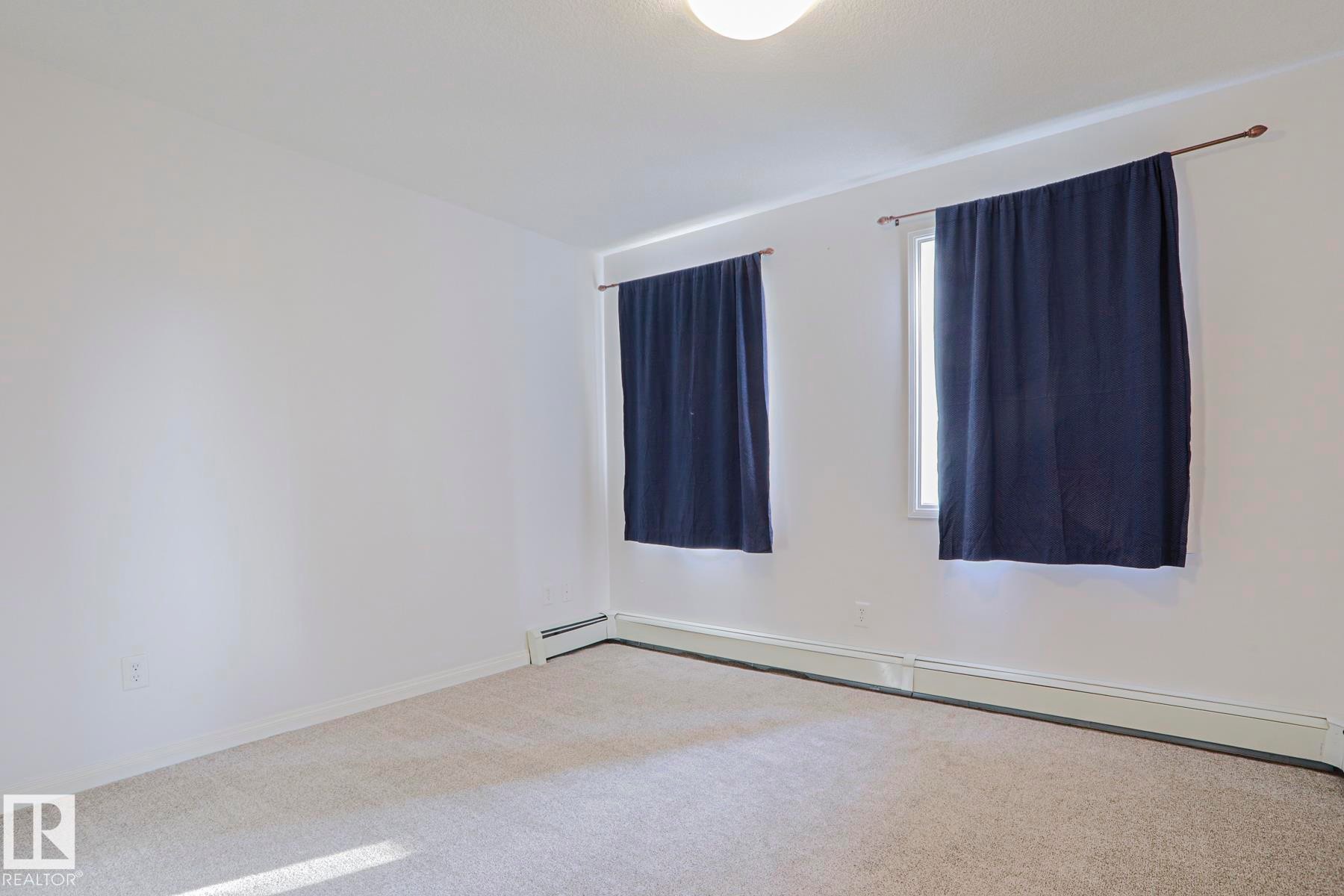 Carpeted flooring with white wall finishes, two windows, and baseboard heating - #108 1204 156 St Nw, Edmonton, AB