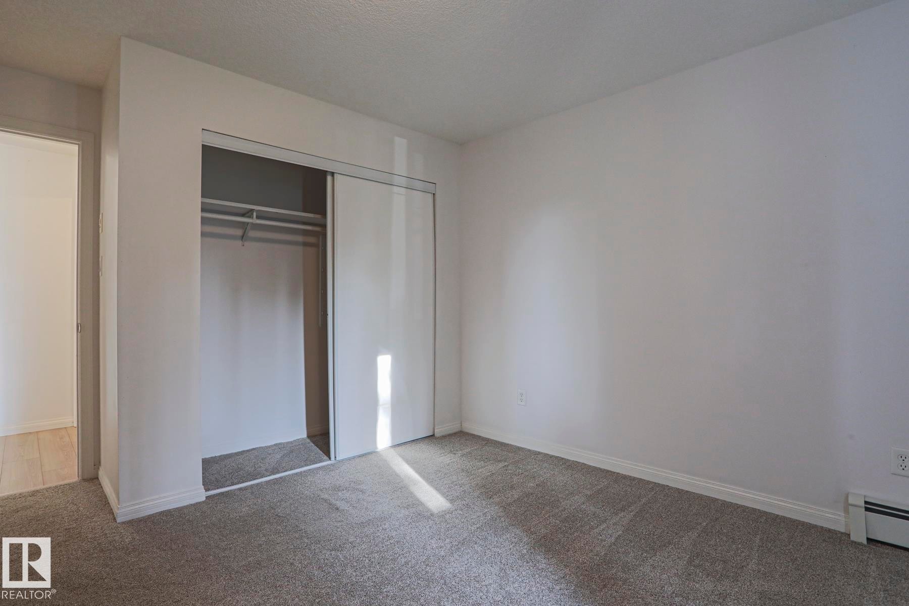 Neutral gray carpeting, white walls, and a built-in closet with sliding doors - #108 1204 156 St Nw, Edmonton, AB