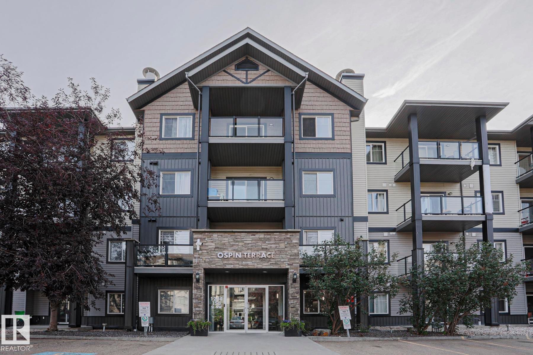 Contemporary multi-story building featuring stone veneer accents, multiple balconies with glass railings, and a prominent main entrance - #108 1204 156 St Nw, Edmonton, AB