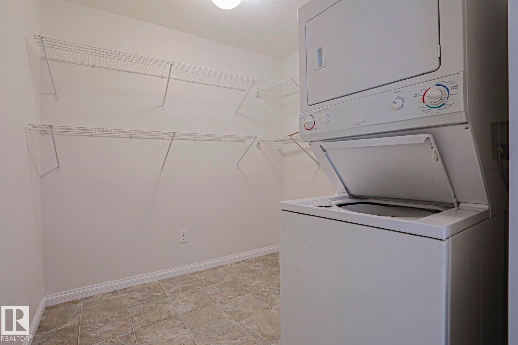 Dedicated utility space featuring a stacked washer and dryer, tile flooring, and multiple wire shelving units - #108 1204 156 St Nw, Edmonton, AB