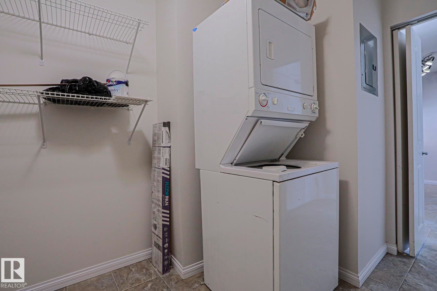 Stacked laundry appliances, wire shelving, and tiled flooring - #108 1204 156 St Nw, Edmonton, AB