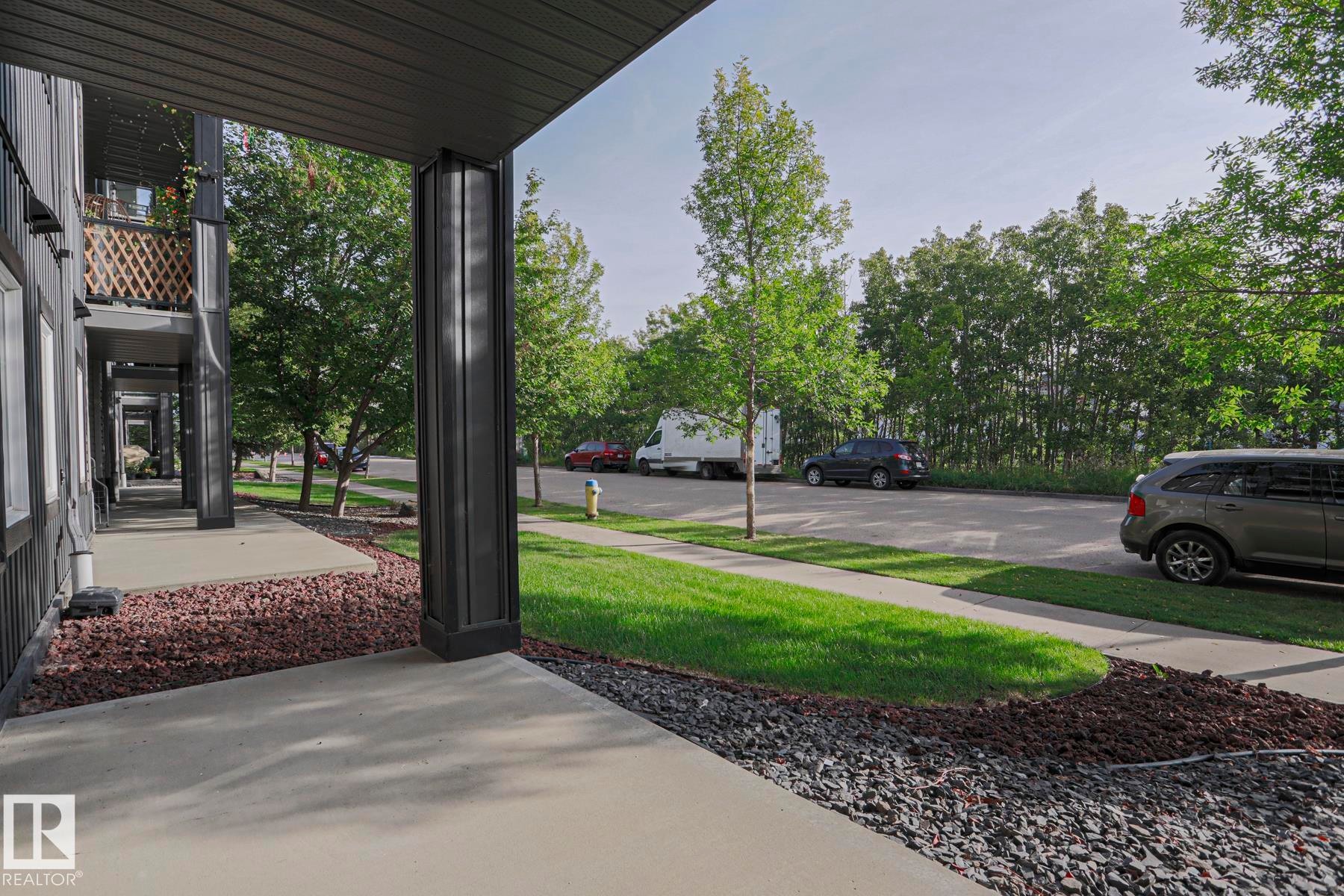 Exterior corridor with concrete walkway, black siding, and decorative gravel landscaping - #108 1204 156 St Nw, Edmonton, AB