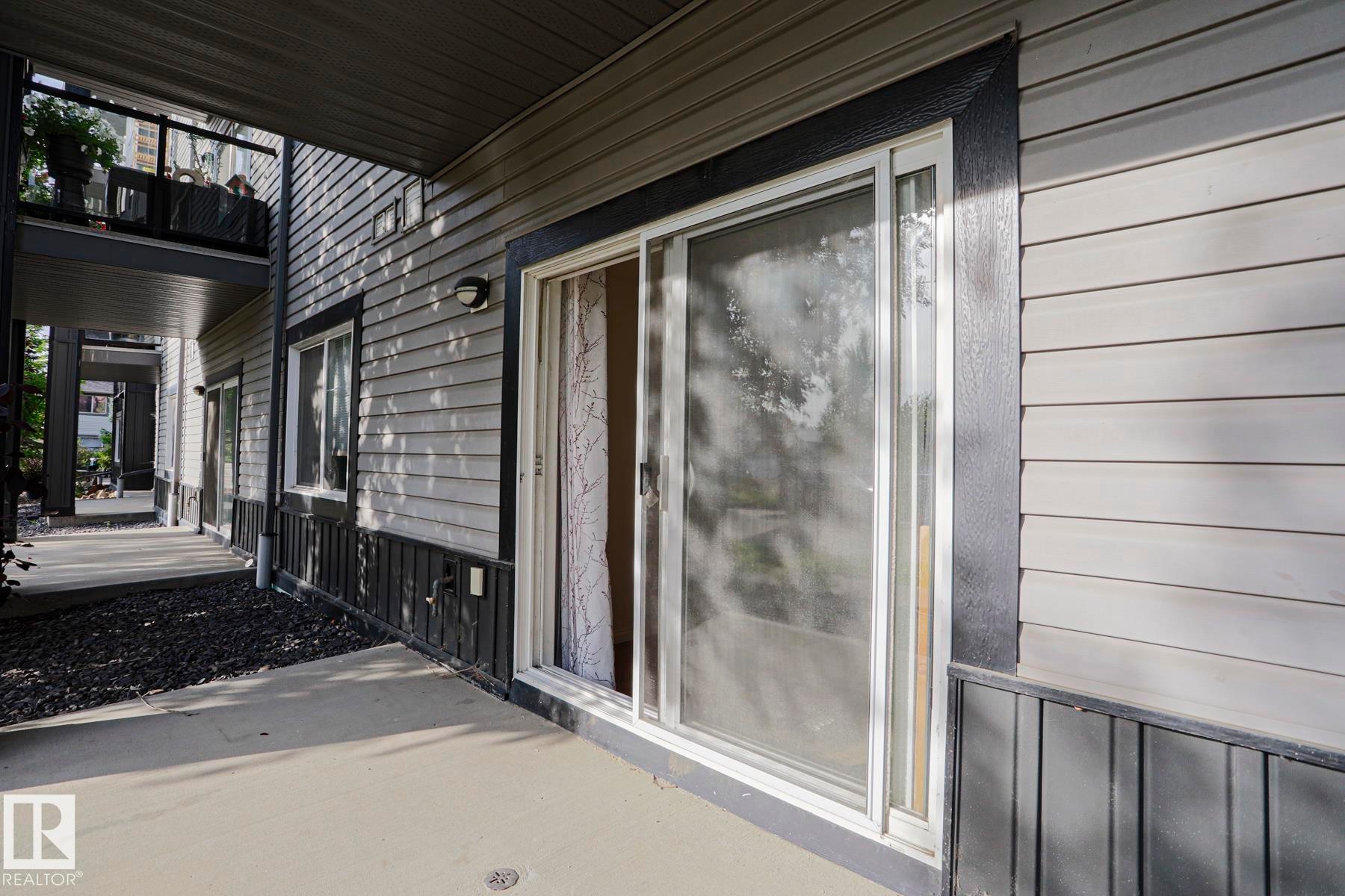 Patio with a concrete surface, featuring a sliding glass door, horizontal siding, and a wall-mounted light fixture - #108 1204 156 St Nw, Edmonton, AB