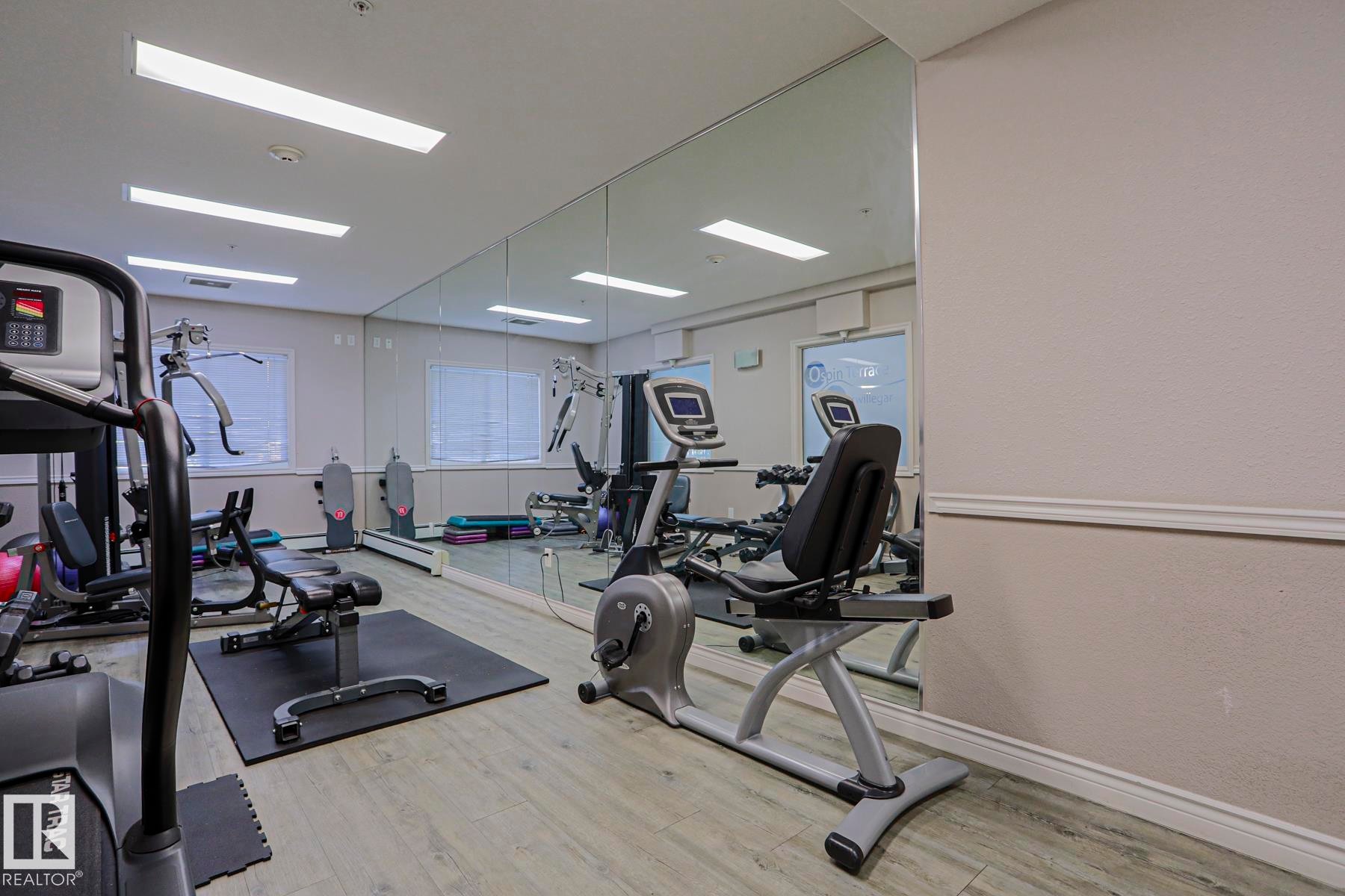 Fitness room featuring full-wall mirrors, wood-finish flooring, and recessed lighting - #108 1204 156 St Nw, Edmonton, AB