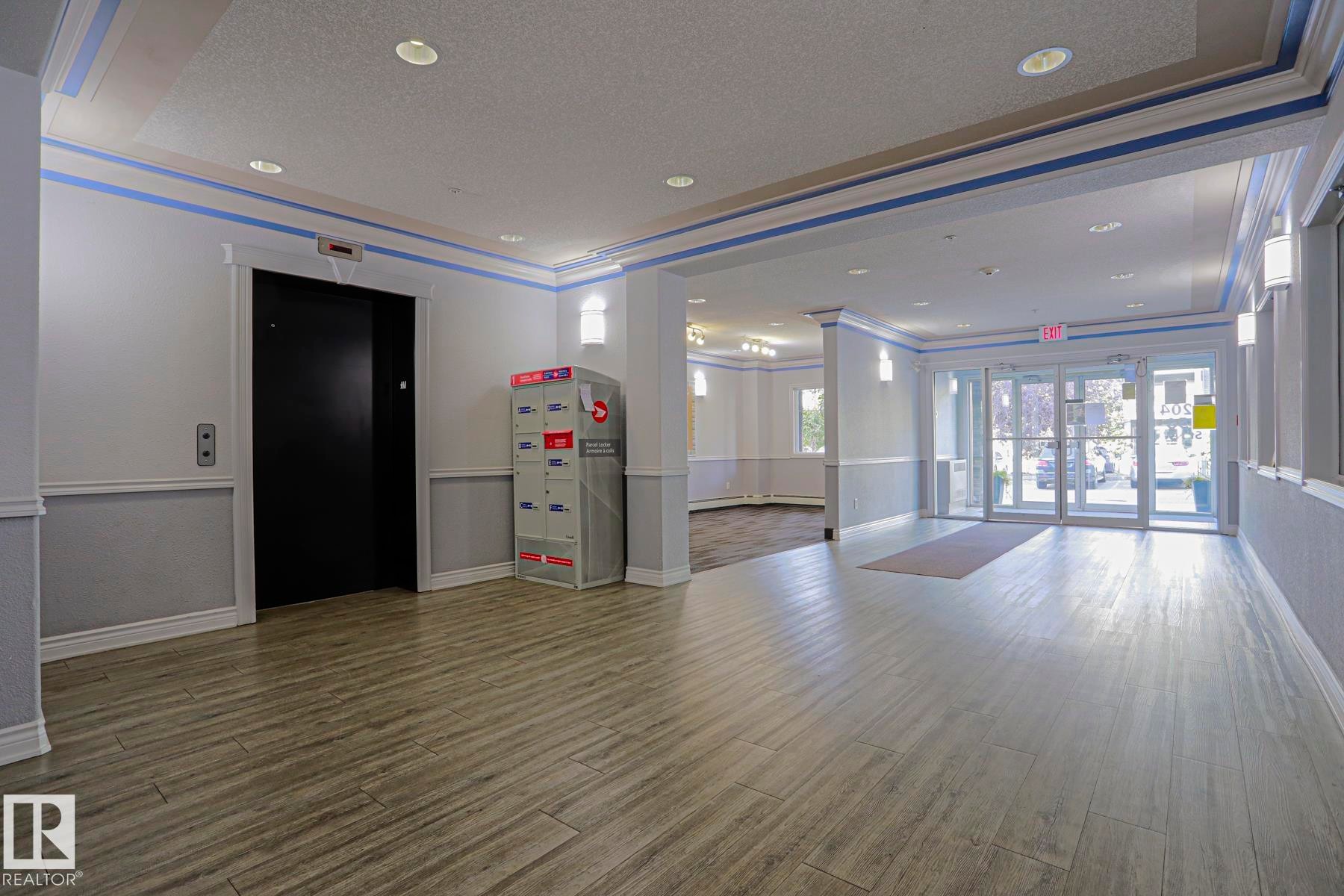 Lobby area featuring wood-finish flooring, recessed lighting, wall sconces, and a black elevator door - #108 1204 156 St Nw, Edmonton, AB