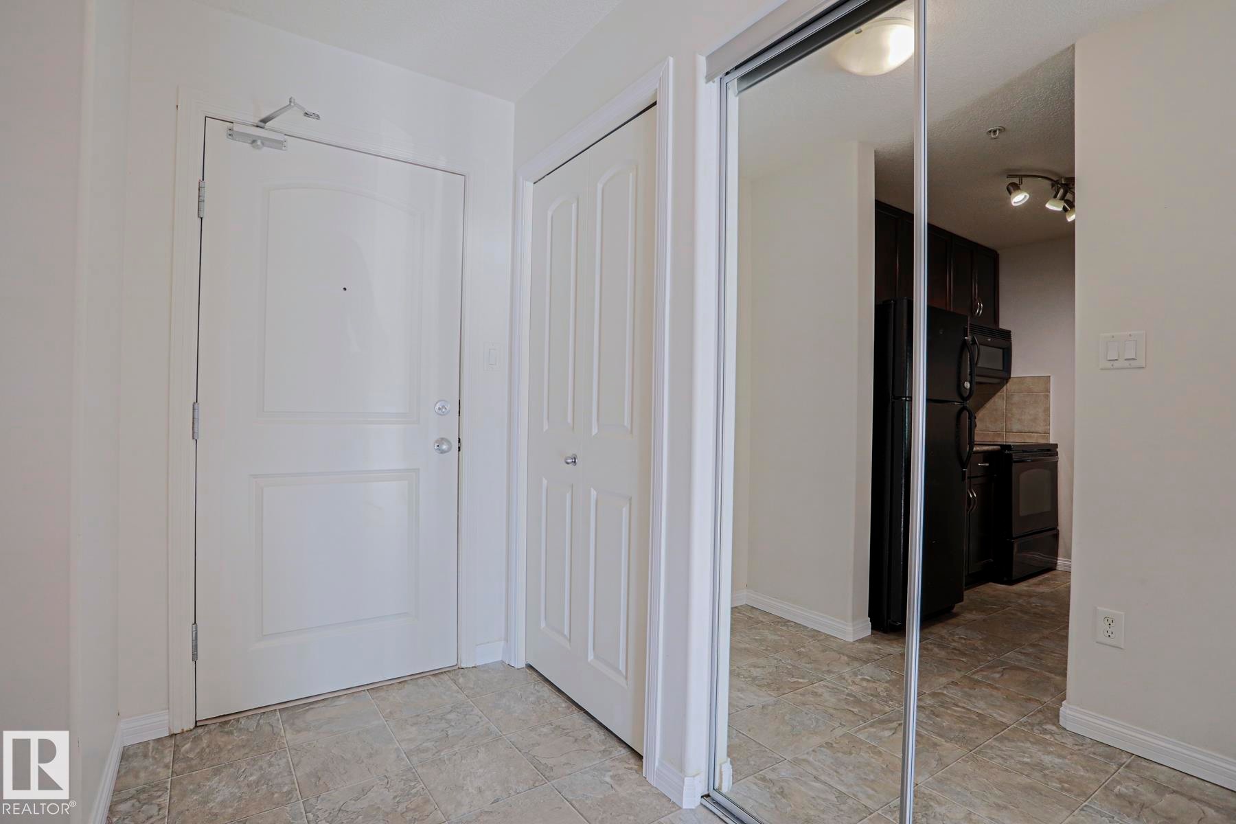Tiled flooring, white paneled door, built-in mirrored closet, track lighting, and dark wood-finish cabinetry - #108 1204 156 St Nw, Edmonton, AB