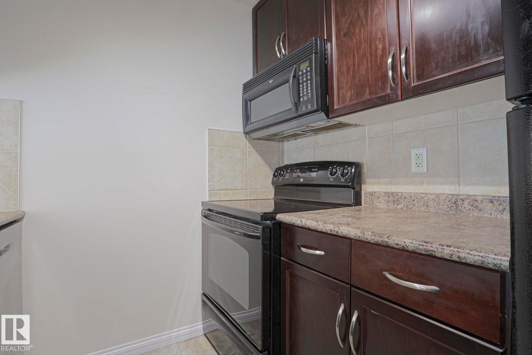 Dark wood-finish cabinetry, light-toned countertops, and a tile backsplash - #108 1204 156 St Nw, Edmonton, AB