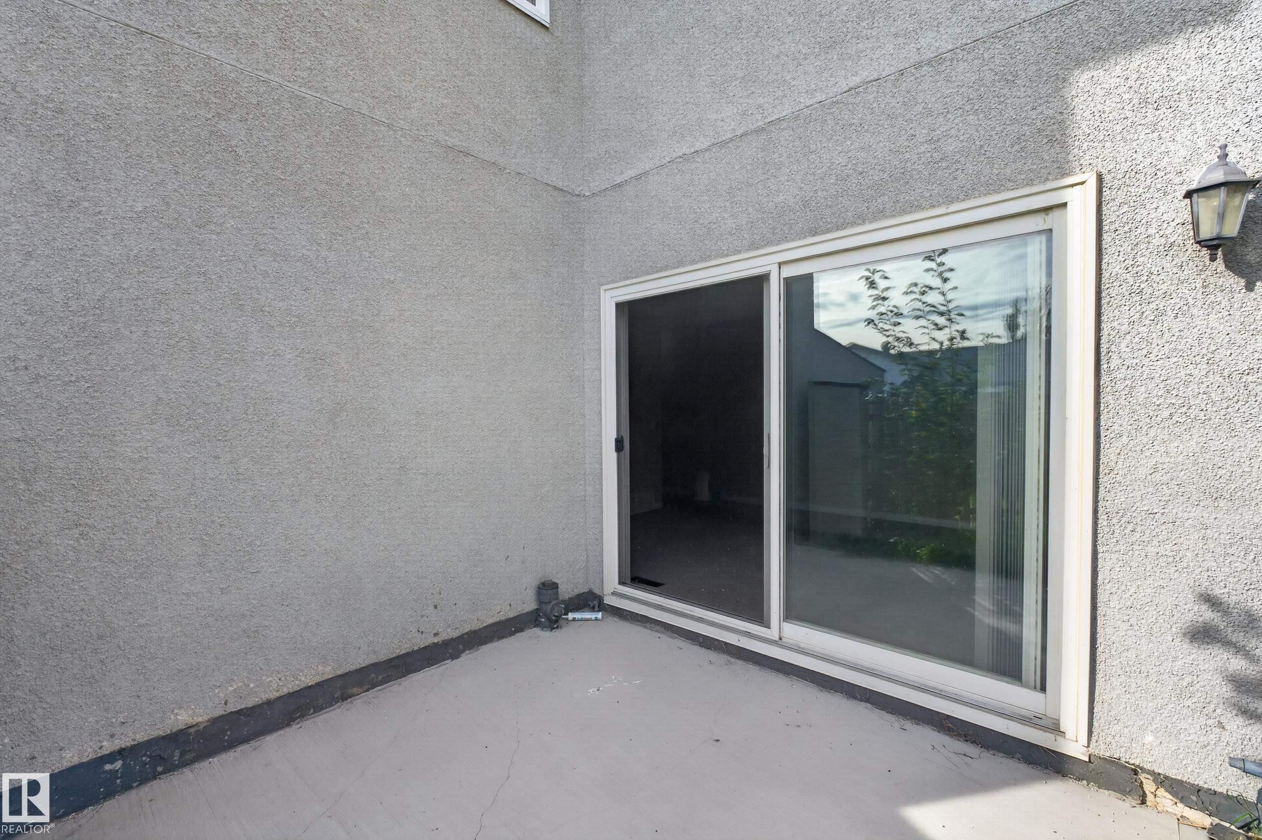 Concrete patio with a stucco exterior, featuring a sliding glass door and an exterior wall lantern - 17749 95 Street Nw, Edmonton, AB