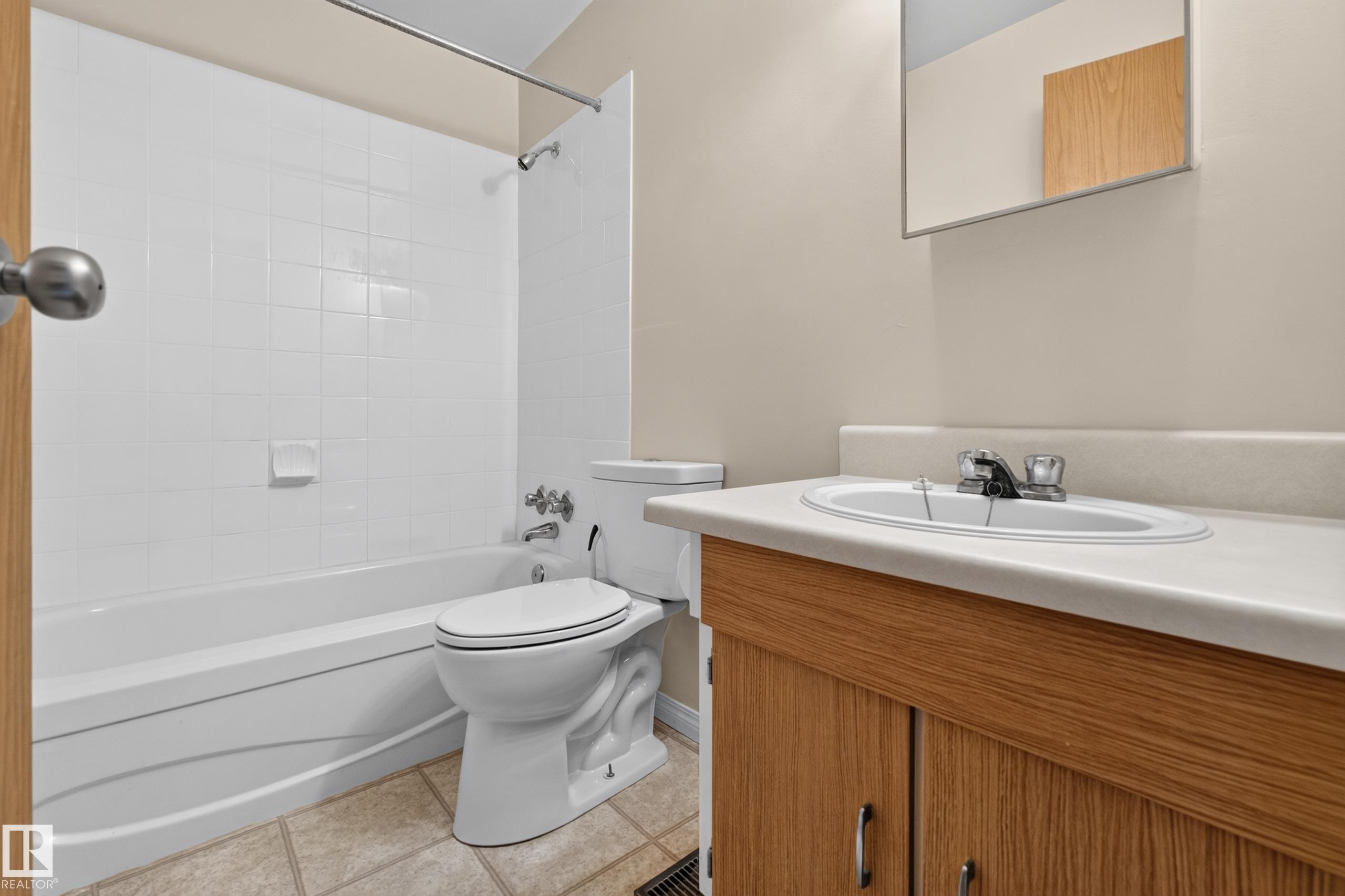 White tiled shower surround, integrated tub, light wood-finish vanity, integrated sink, and wall-mounted mirror - 17749 95 Street Nw, Edmonton, AB