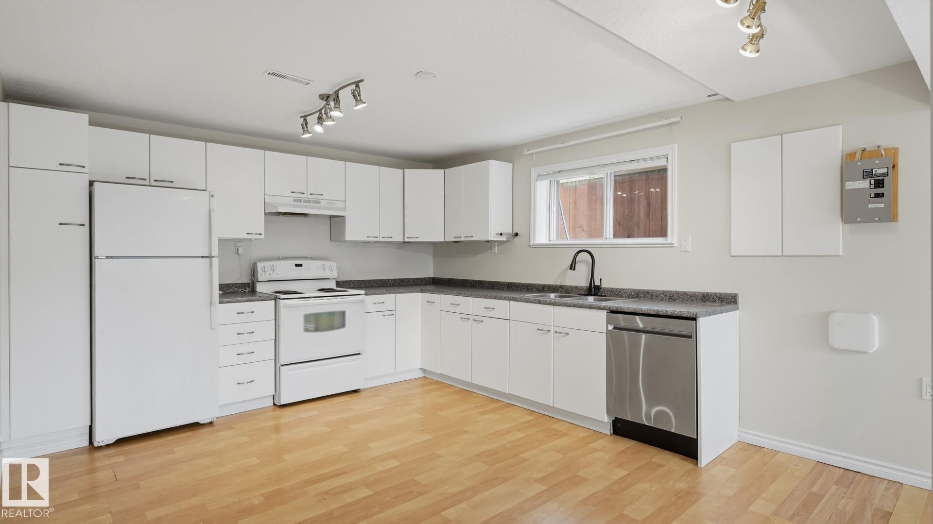 Kitchen featuring wood-finish flooring, white cabinetry, integrated range with overhead hood, and a stainless steel dishwasher - 12208 146 Avenue Nw, Edmonton, AB