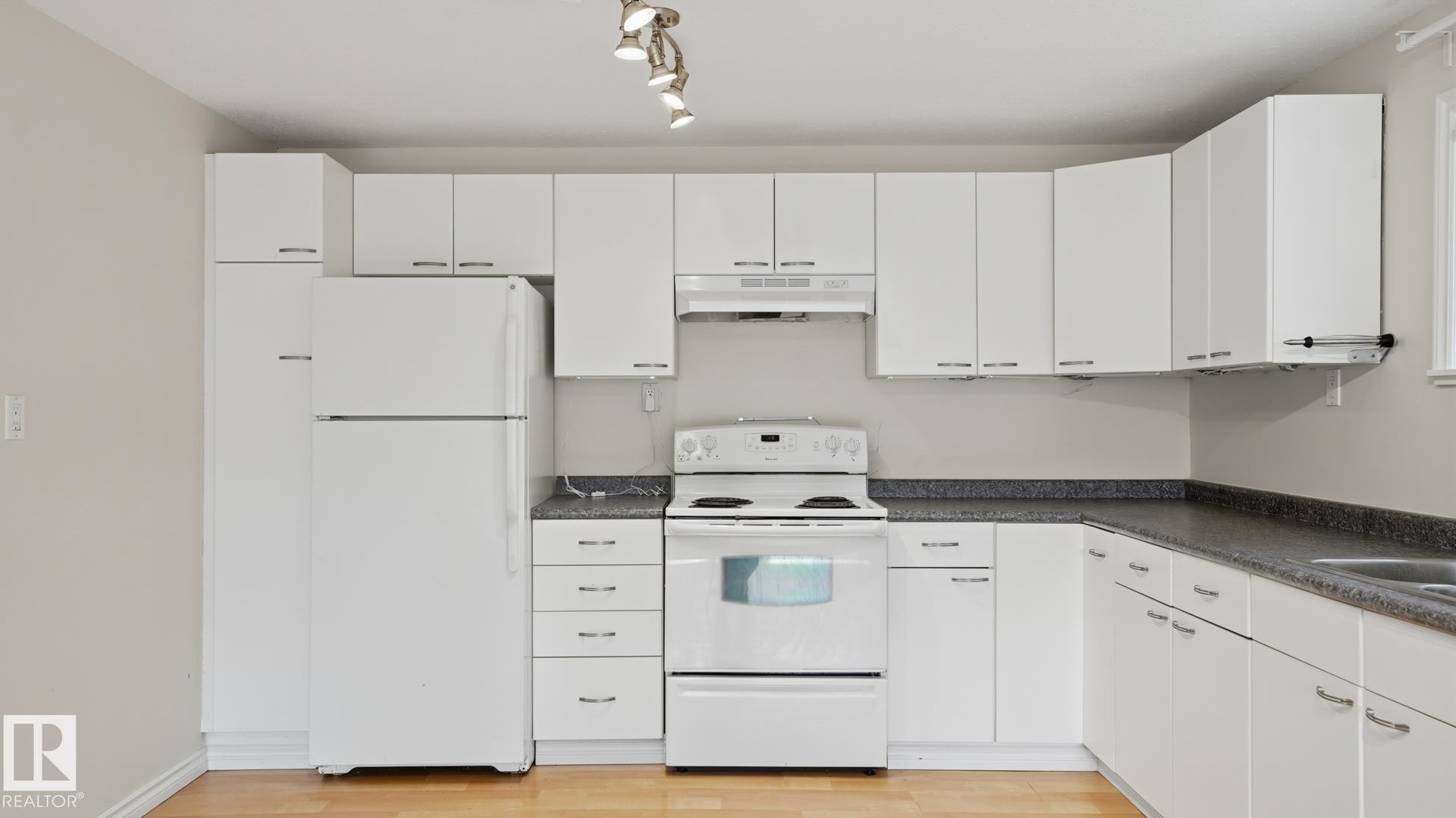 Kitchen featuring white cabinetry, dark speckled countertops, white appliances, track lighting, and wood-finish flooring - 12208 146 Avenue Nw, Edmonton, AB