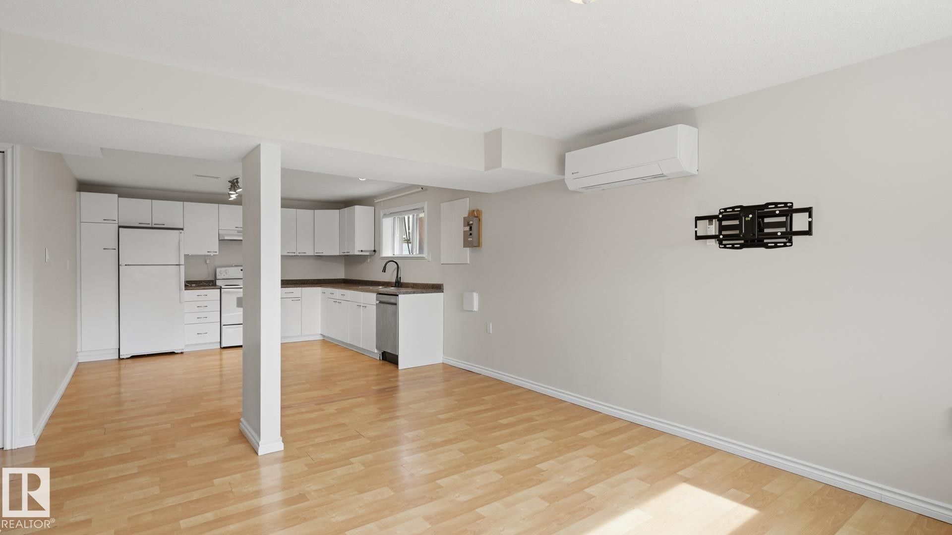 Open-concept living space featuring wood-finish flooring, white cabinetry, a built-in dishwasher, and an installed wall-mounted air conditioning unit - 12208 146 Avenue Nw, Edmonton, AB