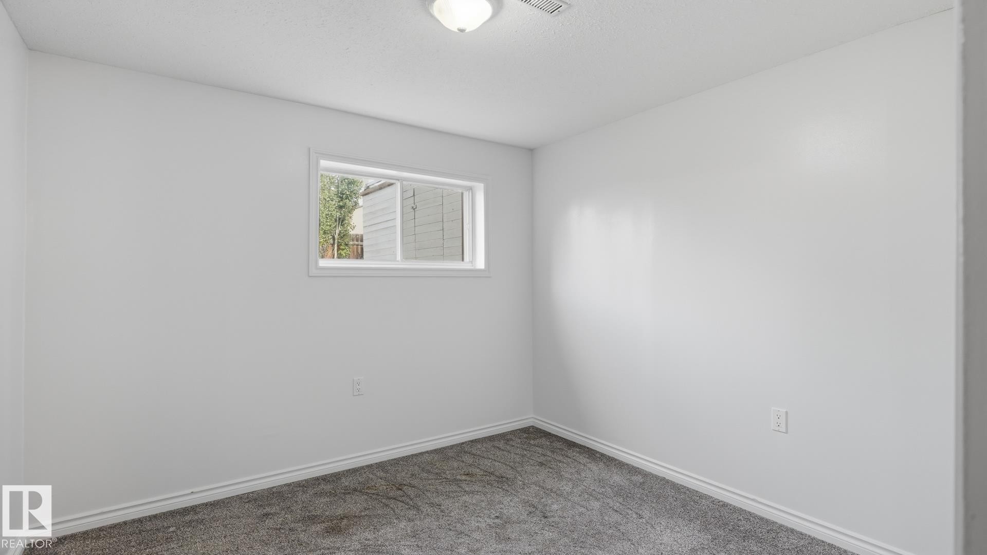 White painted walls, gray carpet flooring, white trim, and a single window with white framing - 12208 146 Avenue Nw, Edmonton, AB