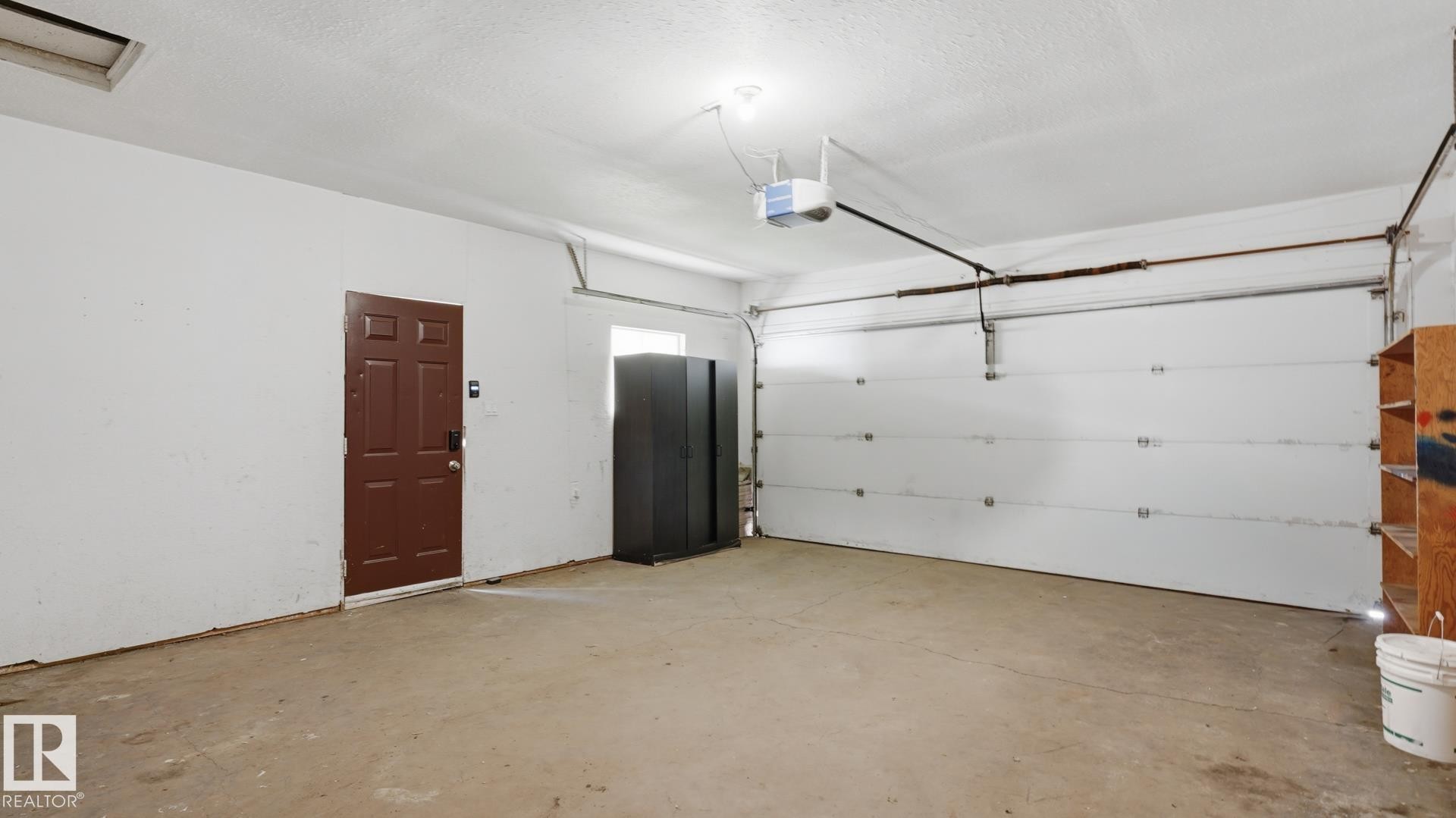 Garage space with concrete flooring, white overhead garage door, and a brown paneled entry door - 12208 146 Avenue Nw, Edmonton, AB