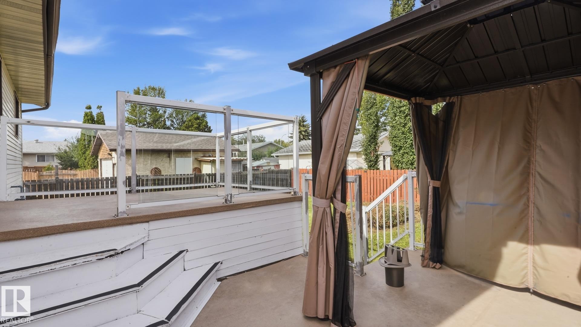 Outdoor deck featuring glass panel railing, white wood stairs, and an attached gazebo with privacy curtains - 12208 146 Avenue Nw, Edmonton, AB