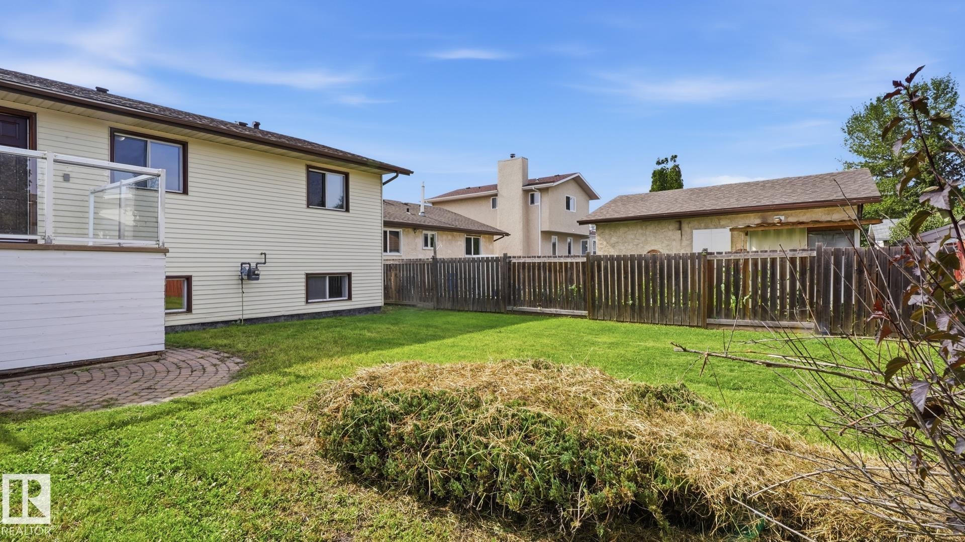 Expansive green space, privacy fencing, upper-level deck with glass railing, lower-level patio with paver stones, and exterior siding - 12208 146 Avenue Nw, Edmonton, AB