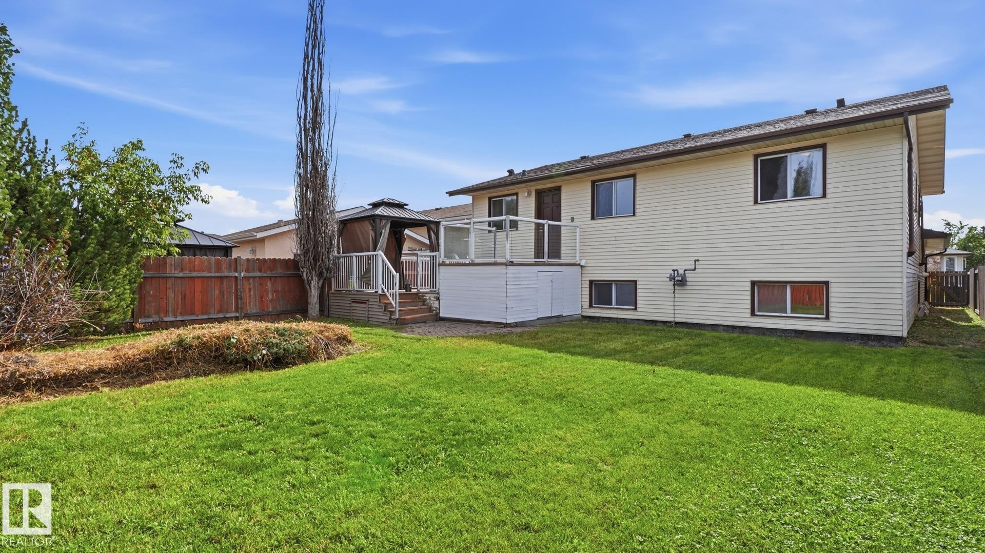Expansive backyard featuring a manicured lawn, a raised deck with glass railings, and a gazebo - 12208 146 Avenue Nw, Edmonton, AB