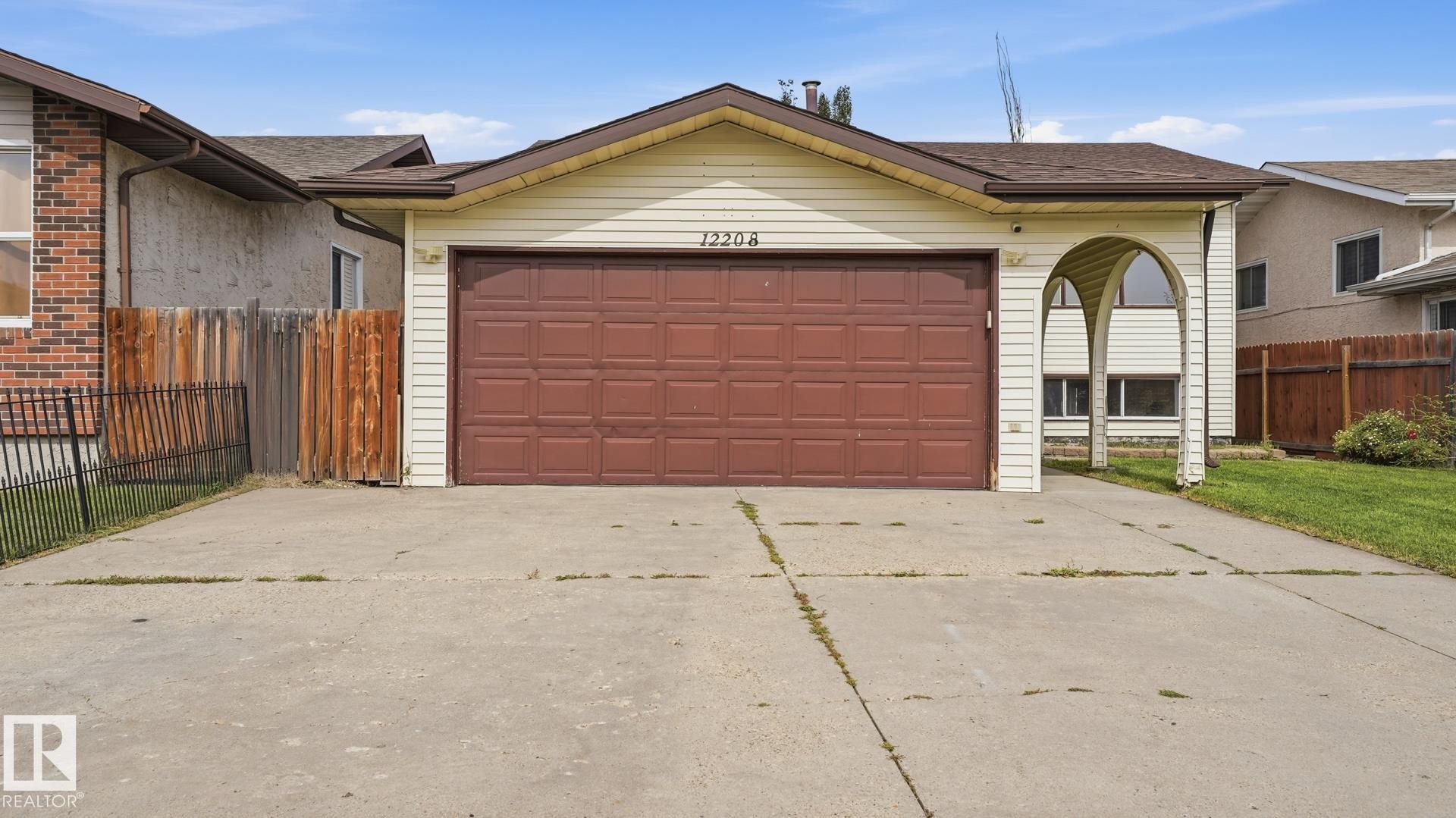 Attached garage with a brown panel door, light-colored siding, and a covered entry with arched supports - 12208 146 Avenue Nw, Edmonton, AB