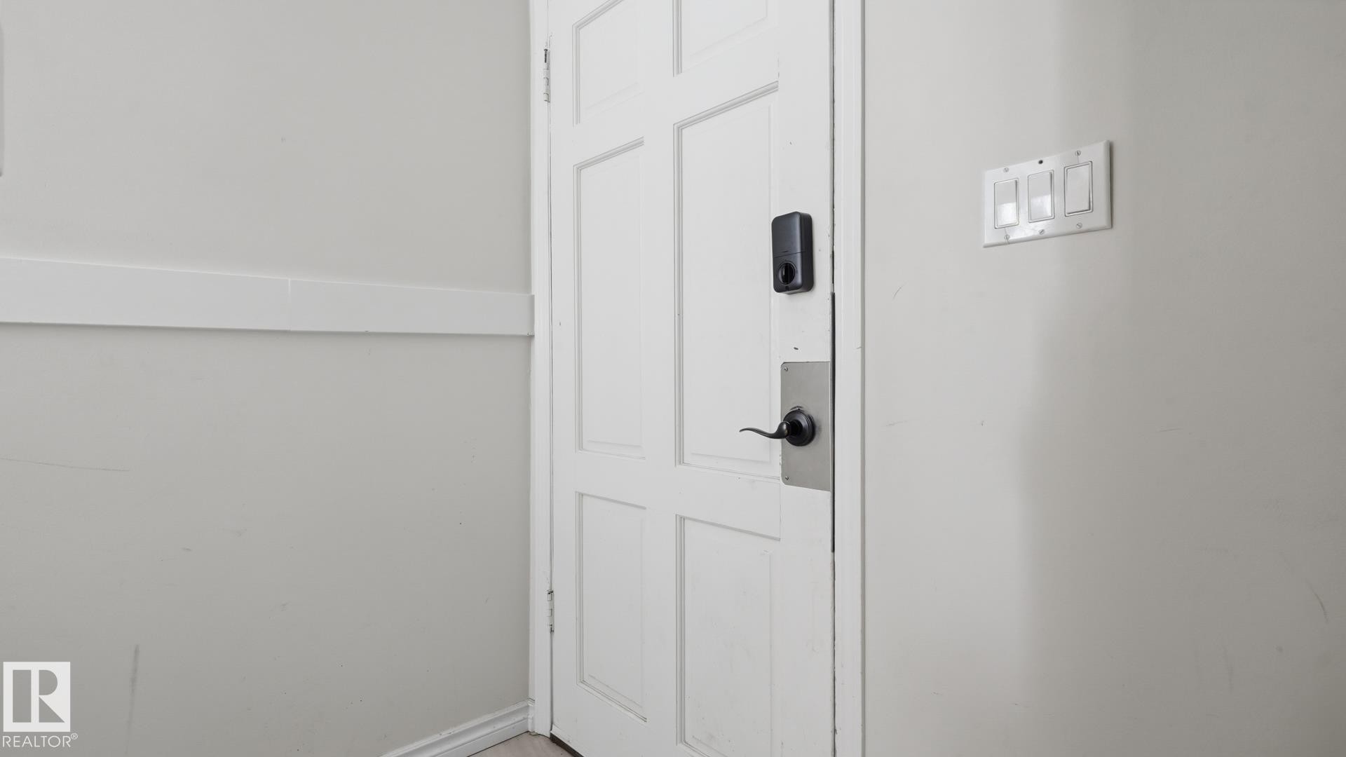 White paneled interior door with black hardware, electronic lock, and adjacent wall-mounted light switches - 12208 146 Avenue Nw, Edmonton, AB