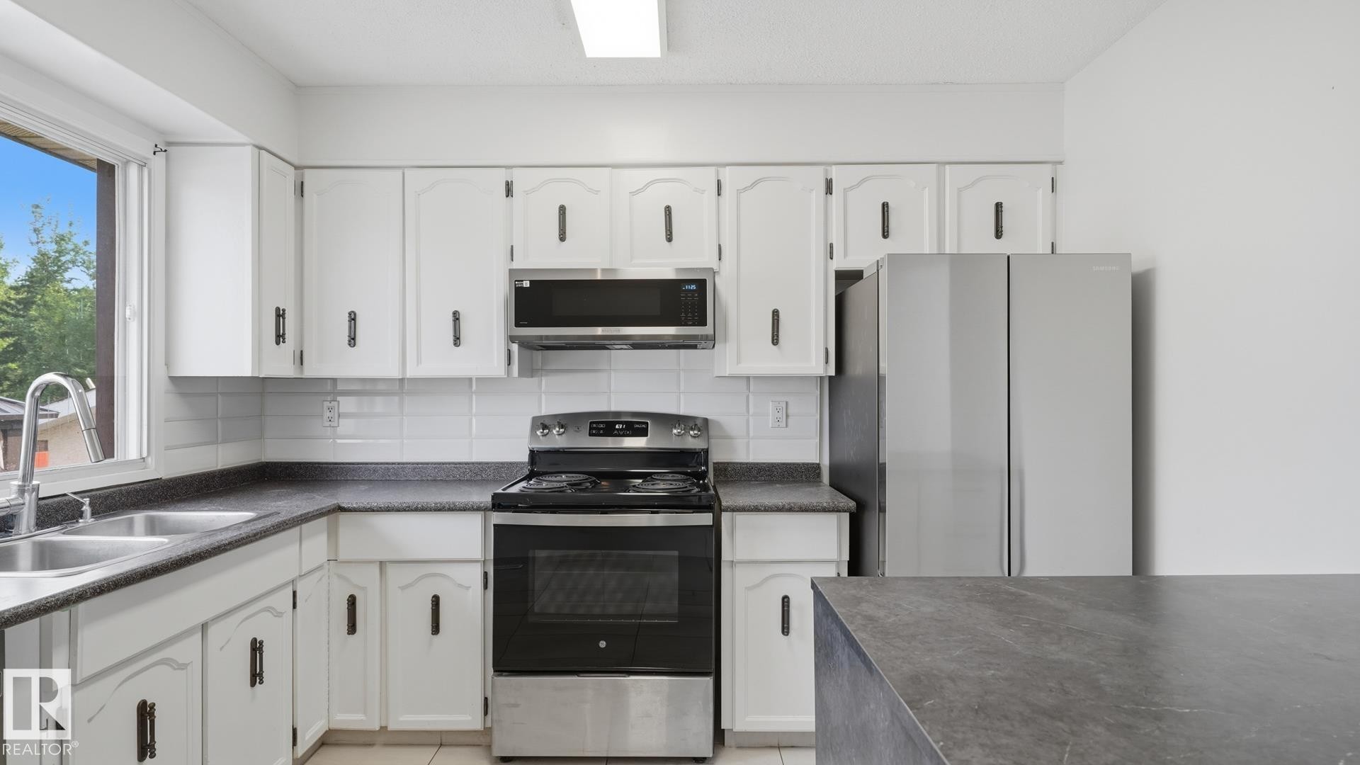 White cabinetry with dark hardware, stainless steel appliances, white tile backsplash, and a double basin sink - 12208 146 Avenue Nw, Edmonton, AB
